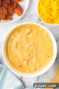 Ultimate Nacho Cheese Dip 10 A large bowl of melted nacho cheese dip, with bowls of shredded cheese and bacon on the side.