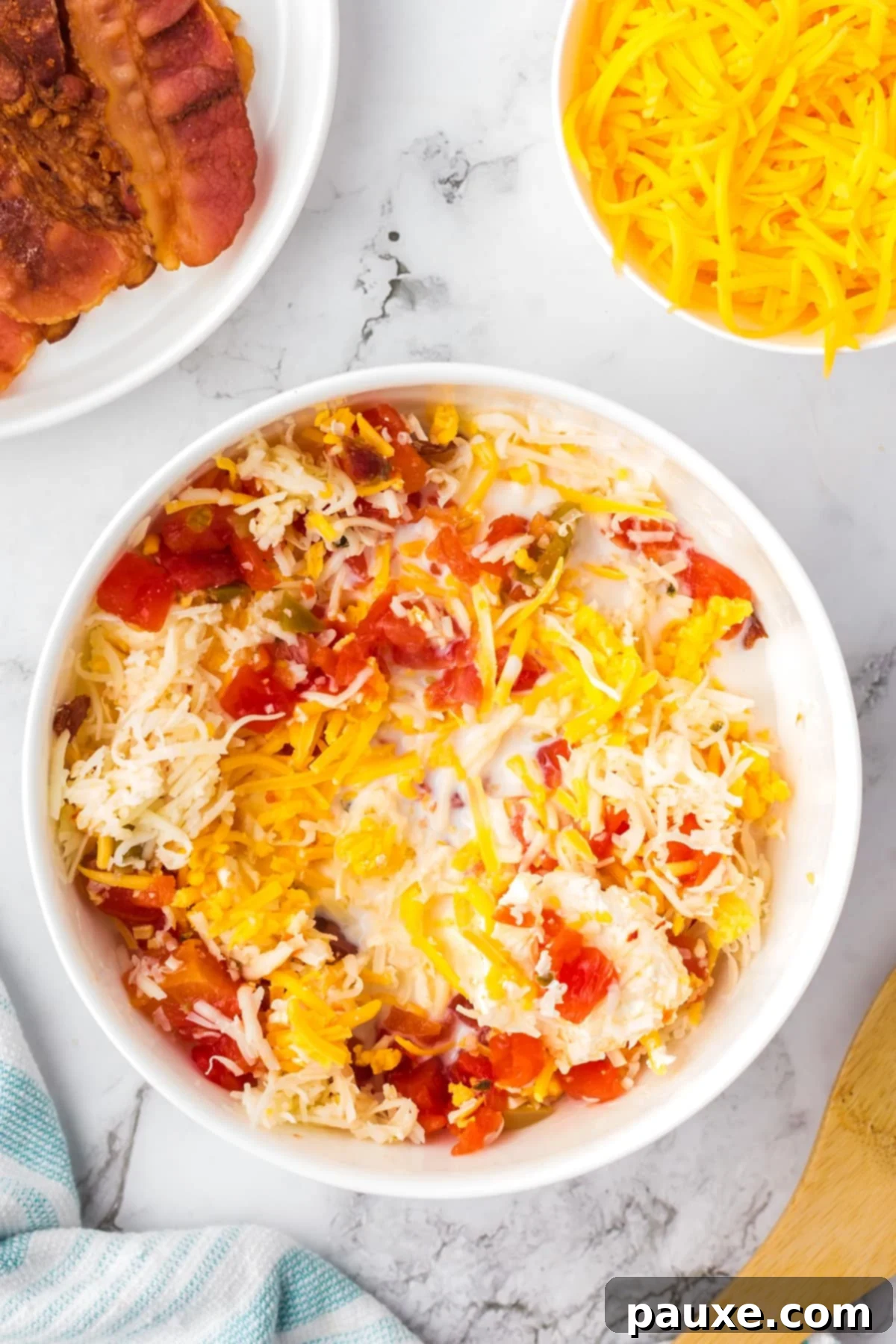 Ultimate Nacho Cheese Dip 5 A large bowl with cheese and cream cheese being mixed together with bacon and rotel tomatoes, partially melted.