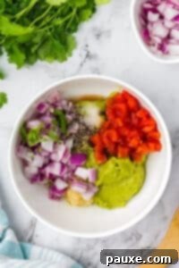 Perfectly Chunky Guacamole 9 A bowl of mashed avocado topped with red onion, tomato, garlic, pepper, salt, and cilantro, before mixing.