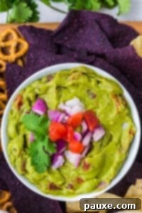 Perfectly Chunky Guacamole 11 A bowl of guacamole topped with chopped tomato and red onion, garnished for serving.