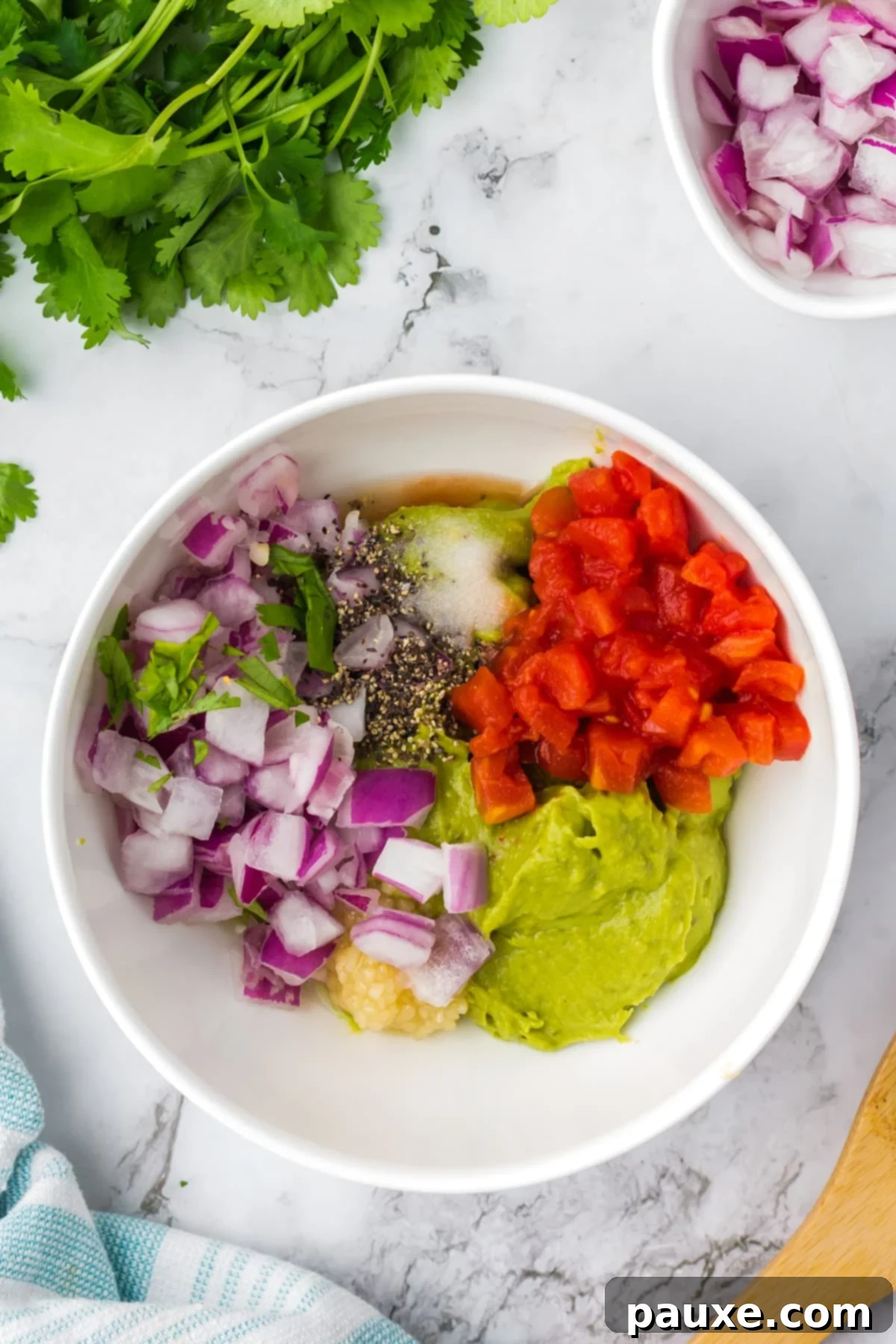 Perfectly Chunky Guacamole 4 A bowl of mashed avocado topped with red onion, tomato, garlic, pepper, salt, and cilantro, ready to be mixed.