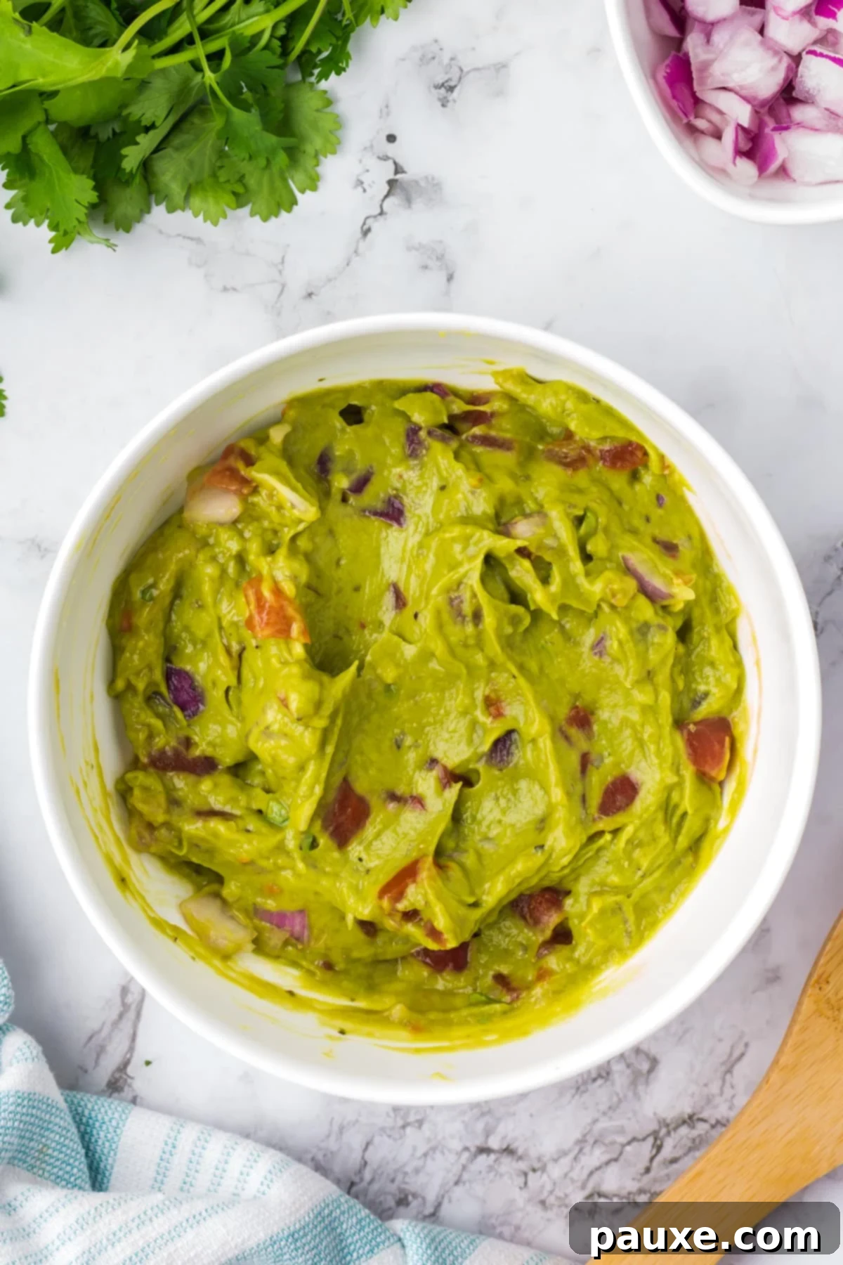 Perfectly Chunky Guacamole 5 A bowl of chunky guacamole with visible pieces of tomato and red onion after mixing.