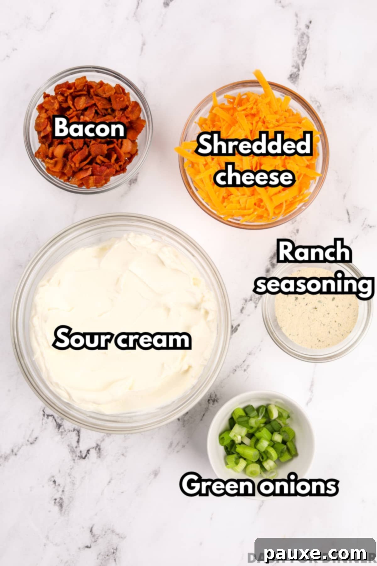 Deconstructed Baked Potato Dip 3 An overhead view of bowls of key ingredients for Loaded Baked Potato Dip, including sour cream, shredded sharp cheddar cheese, crumbled bacon, ranch seasoning, and chopped green onions.