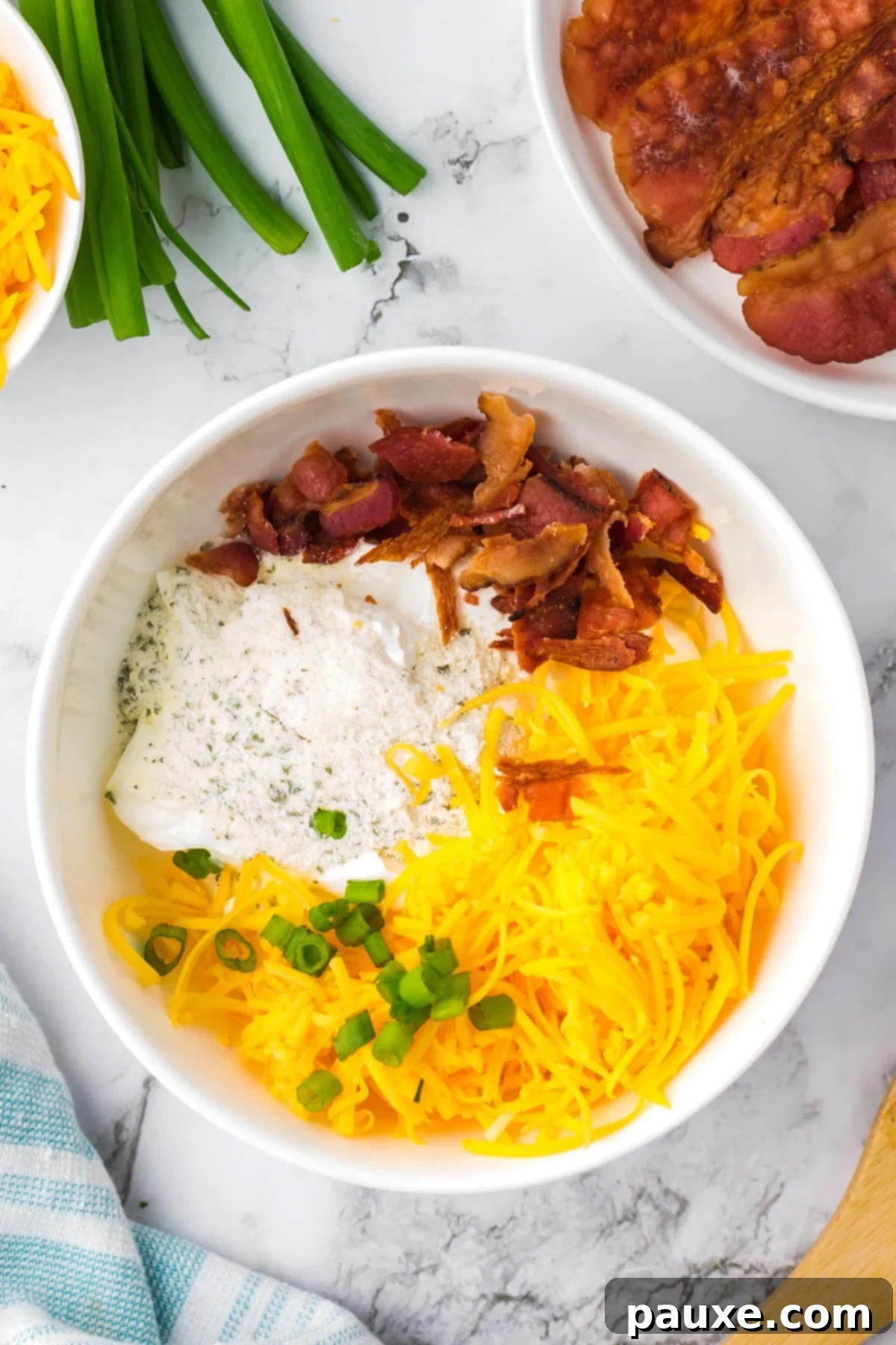 Deconstructed Baked Potato Dip 4 A medium-sized white bowl filled with sour cream, ranch seasoning, shredded cheddar cheese, crumbled bacon, and chopped green onions before mixing.