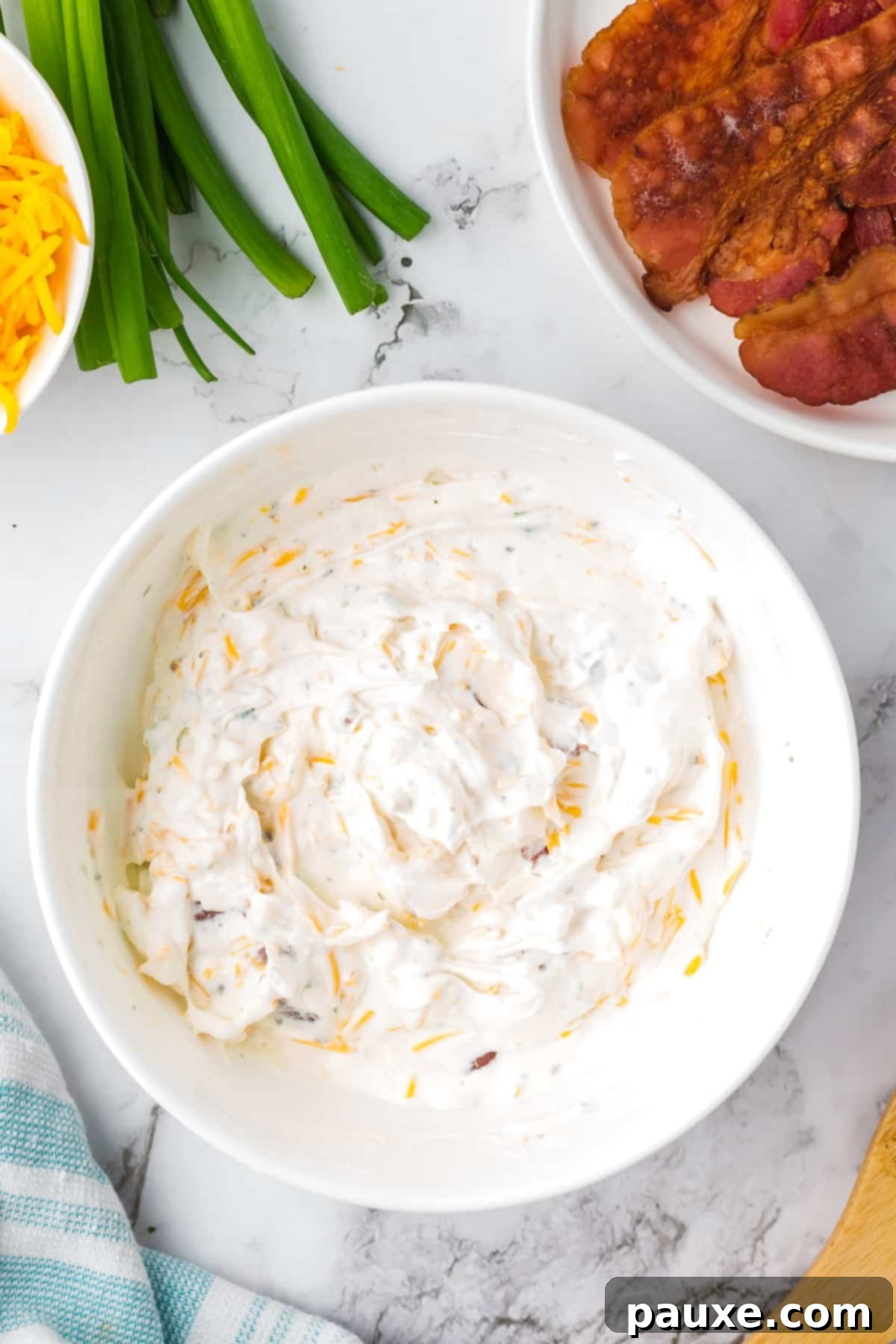 Deconstructed Baked Potato Dip 5 A creamy, smooth bowl of mixed baked potato dip, with separate bowls of cooked bacon and shredded cheese on the side for garnish.