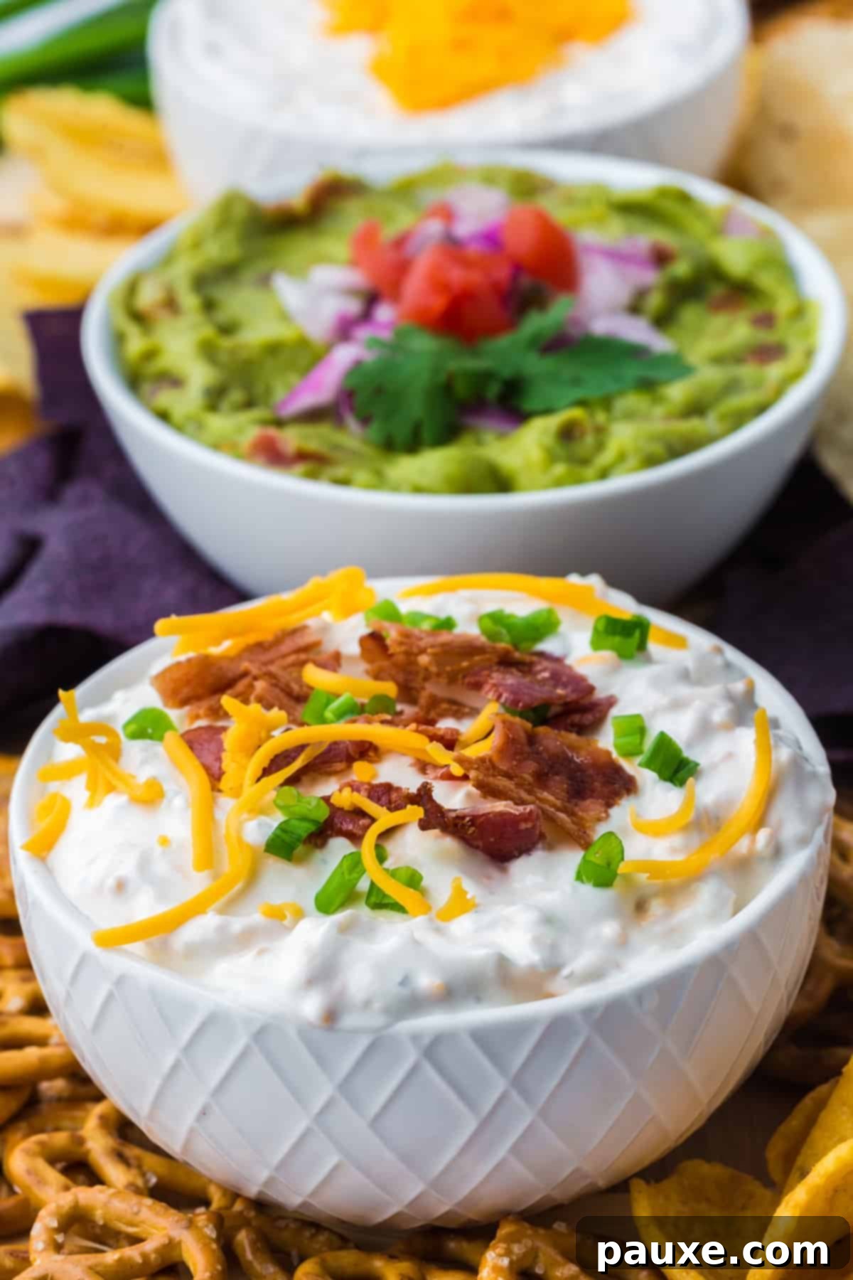 Deconstructed Baked Potato Dip 7 A small, elegant white bowl brimming with Loaded Baked Potato Dip, artfully garnished with vibrant shredded cheddar cheese, savory bacon bits, and fresh green onion.