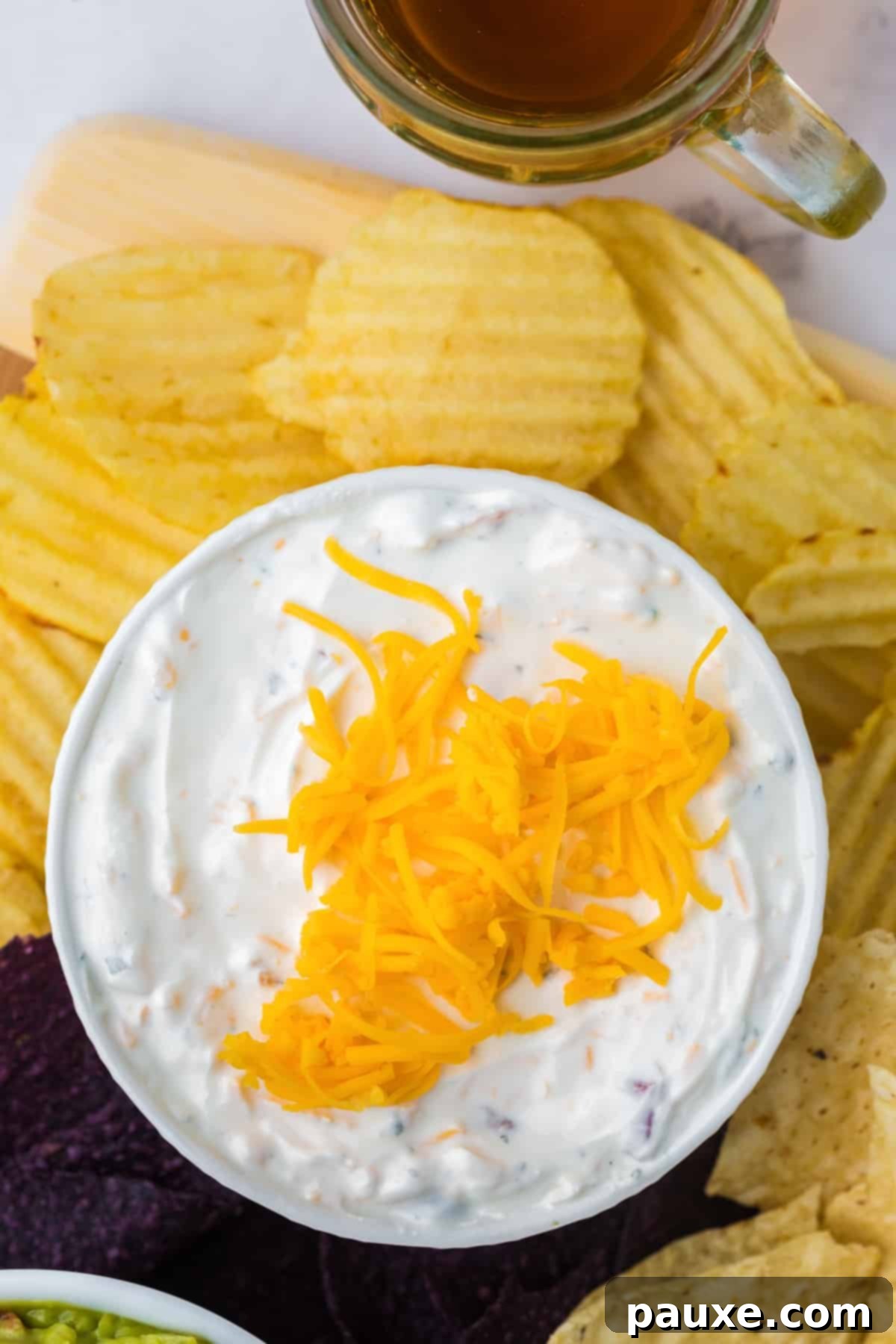 Ultimate Beer Cheese Dip 2 A beautifully presented bowl of creamy cheesy beer dip, generously topped with shredded cheddar cheese, surrounded by a pile of ruffled potato chips ready for dipping.