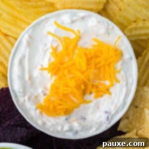 Ultimate Beer Cheese Dip 8 A bowl of creamy beer dip, topped with a generous sprinkle of shredded cheese, with various chips arranged around the sides, ready for serving.