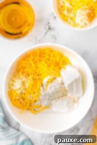 Ultimate Beer Cheese Dip 9 A bowl filled with softened cream cheese, cheese, and ranch seasoning, with a small cup of beer in the top left corner, ready for mixing.