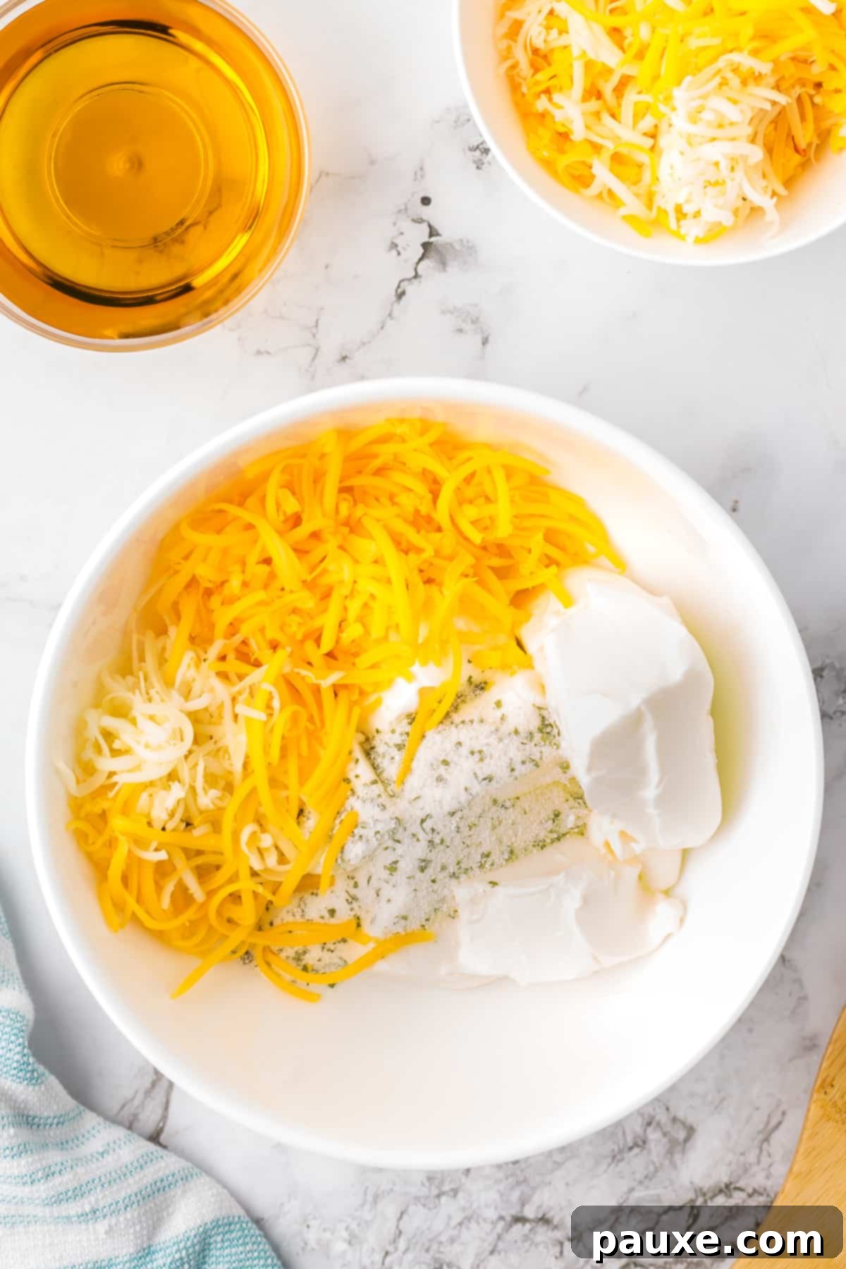 Ultimate Beer Cheese Dip 4 A mixing bowl filled with softened cream cheese, shredded pepper jack and cheddar cheeses, ranch seasoning, and a small glass of beer ready to be mixed.