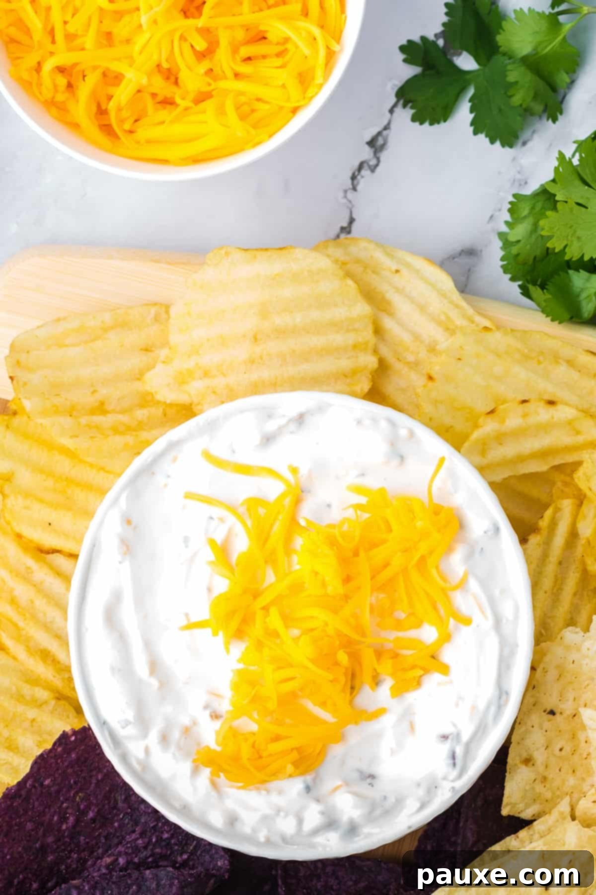Ultimate Beer Cheese Dip 7 A small white bowl filled with creamy cheesy beer dip, topped with shredded cheddar, served alongside a pile of ridged potato chips for dipping.