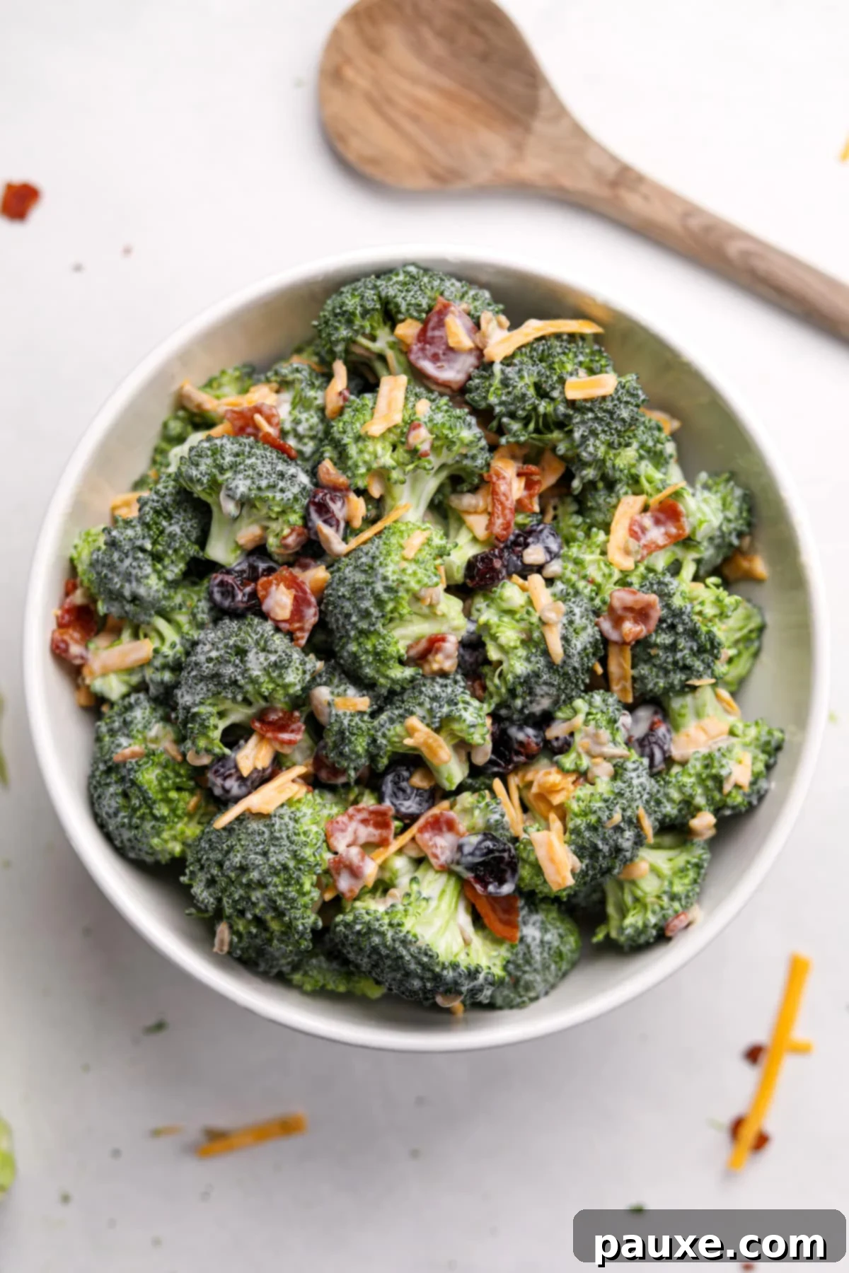 Creamy Crunch Broccoli Salad 11 A pristine white bowl filled with a freshly prepared broccoli salad, elegantly garnished with extra crispy bacon and shredded cheddar cheese.
