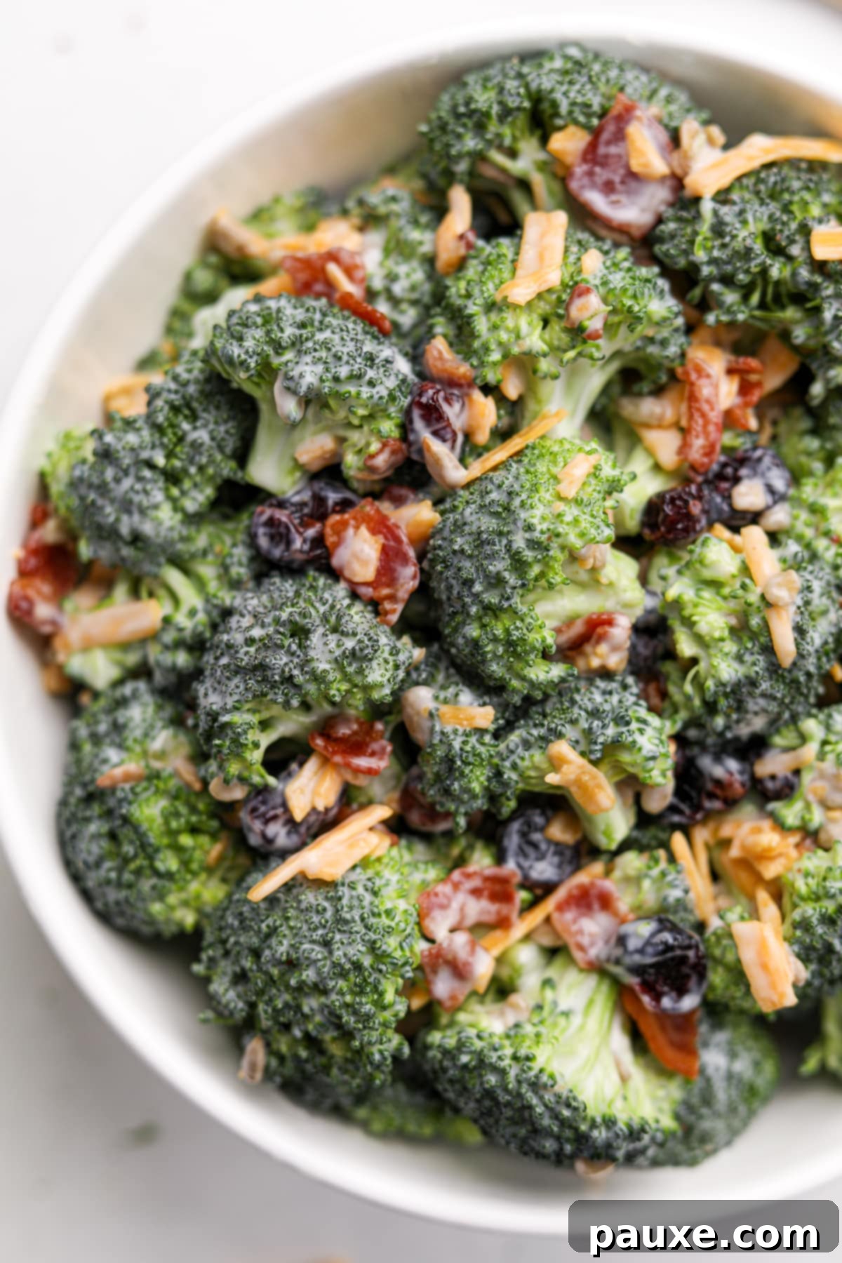 Creamy Crunch Broccoli Salad 12 A detailed close-up of a bowl of broccoli salad, showcasing crispy bacon crumbles and delicate cheddar cheese shreds nestled among the vibrant green broccoli florets.