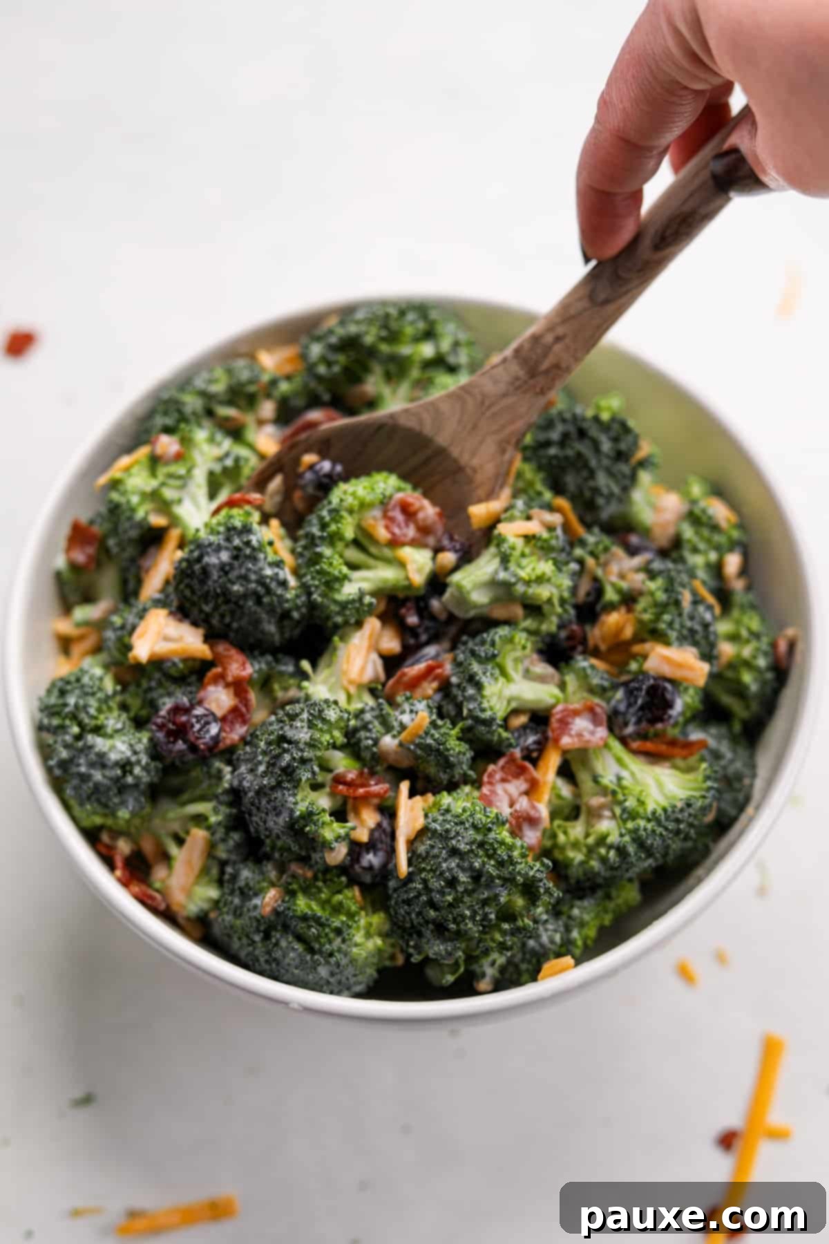 Creamy Crunch Broccoli Salad 13 A wooden spoon actively stirring a large bowl of creamy broccoli salad, highlighting the fresh ingredients and rich dressing.