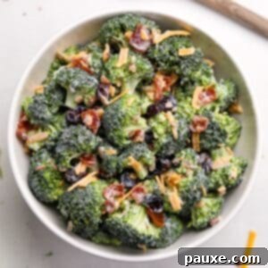 Creamy Crunch Broccoli Salad 15 A white bowl filled with broccoli salad, garnished with cheddar cheese shreds and bacon, ready to be served.