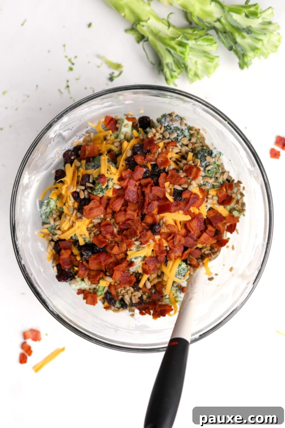Creamy Crunch Broccoli Salad 9 Crispy bacon bits and shredded cheddar cheese being added to the dressed broccoli salad, ready for final mixing.