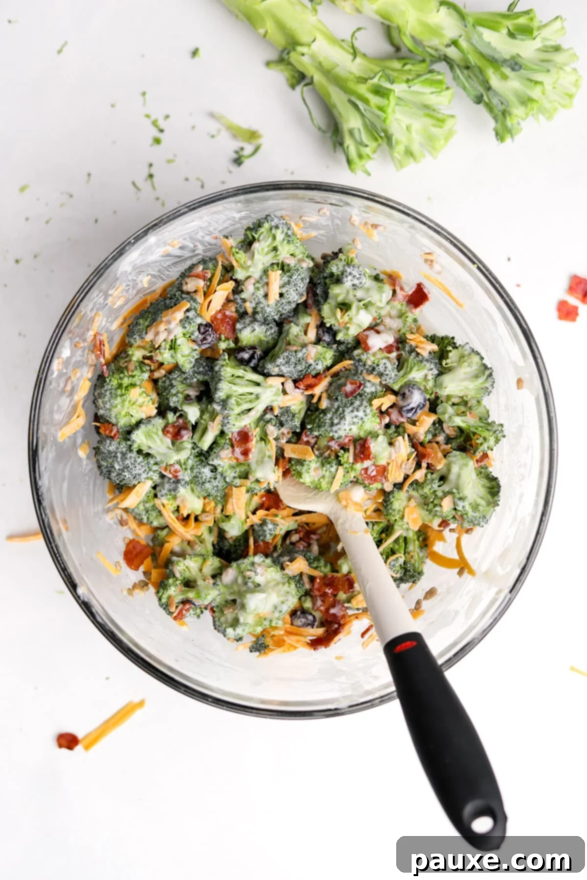 Creamy Crunch Broccoli Salad 10 A large bowl of broccoli salad being gently mixed with a silicone spatula, ensuring all ingredients are evenly distributed.