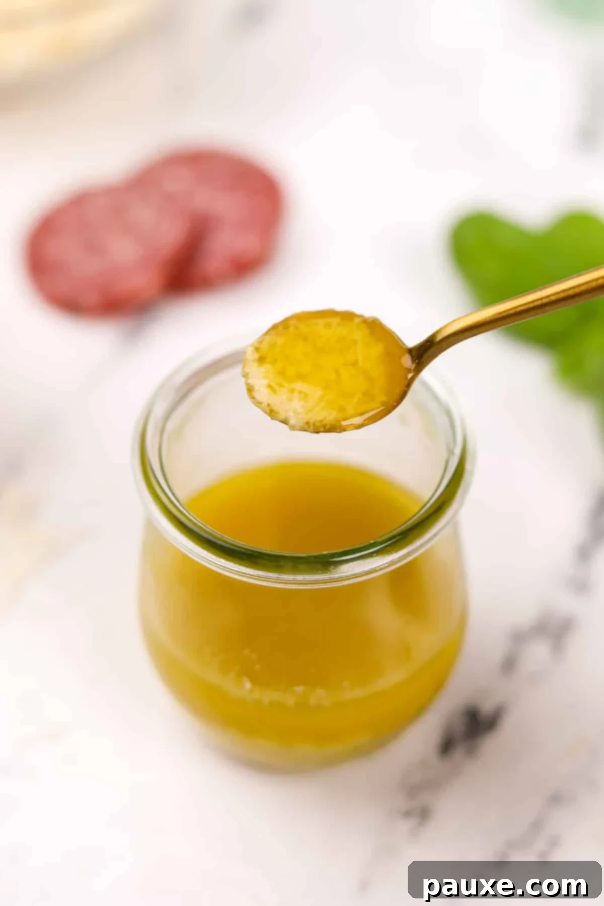 Leon's Signature Dressing 8 A small spoon lifting a glistening amount of homemade vinaigrette from a glass jar, showcasing the dressing's appealing texture.