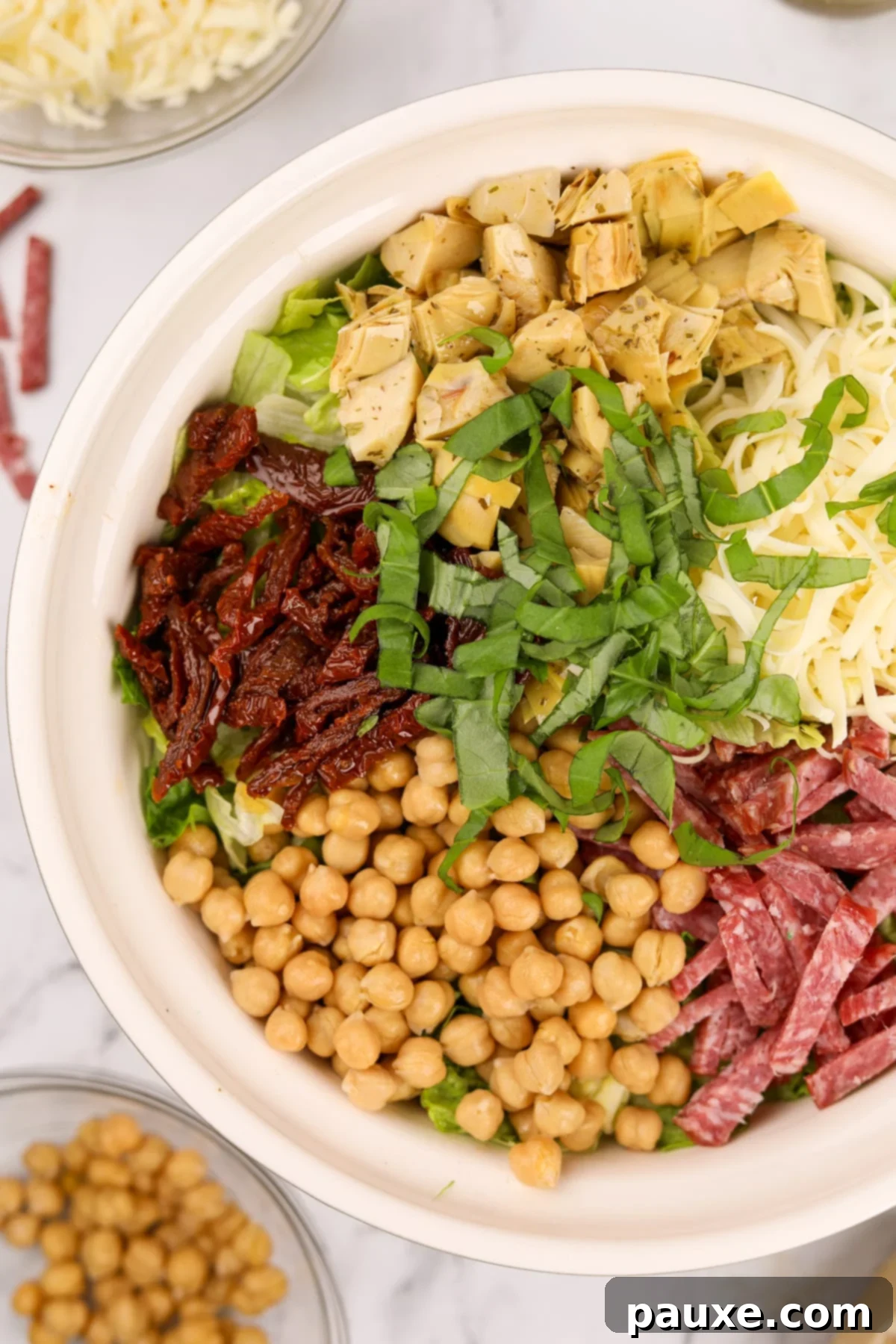 A large bowl of La Scala chopped salad, featuring chickpeas, sun-dried tomatoes, fresh basil, marinated artichokes, mozzarella, and salami, ready to be tossed.