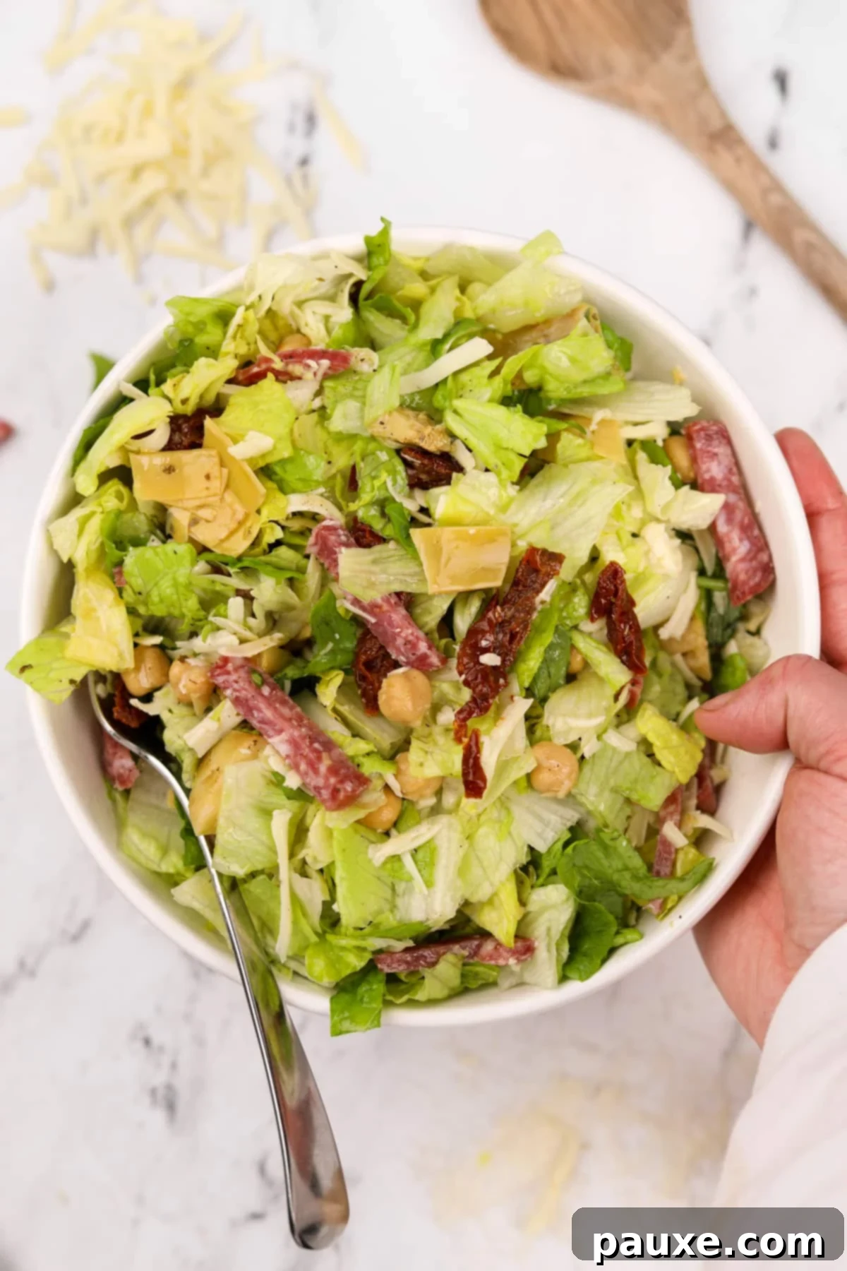 A hand holding a bowl of the vibrant La Scala Chopped Salad, showcasing the perfectly mixed salami and mozzarella.