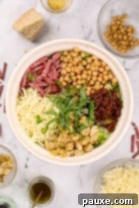A large salad bowl filled with salad, including sections of toppings: mozzarella, artichokes, basil, sun dried tomatoes, chickpeas, and salami.