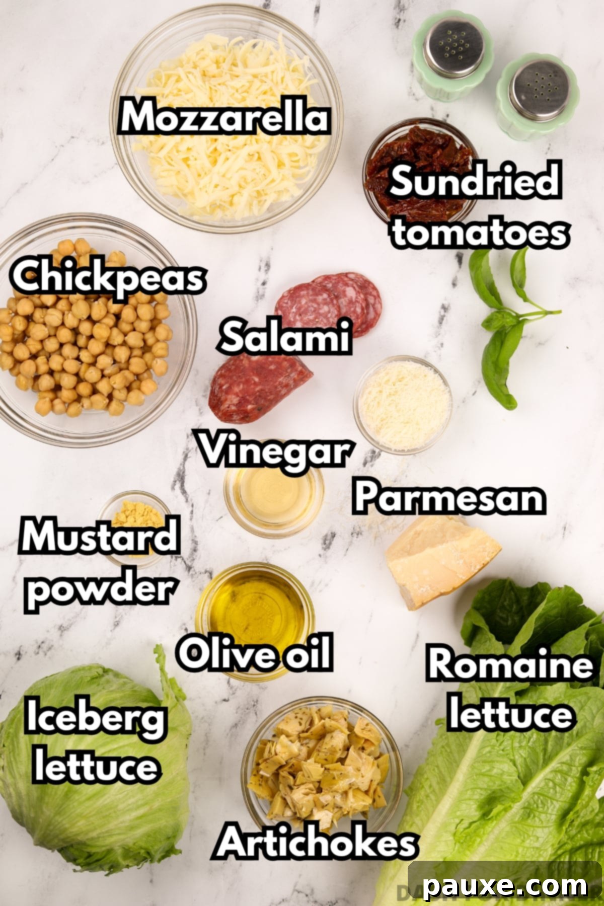 A collection of fresh ingredients laid out for making the La Scala Chopped Salad: salami, chickpeas, mozzarella, sun-dried tomatoes, Parmesan cheese, and fresh greens.