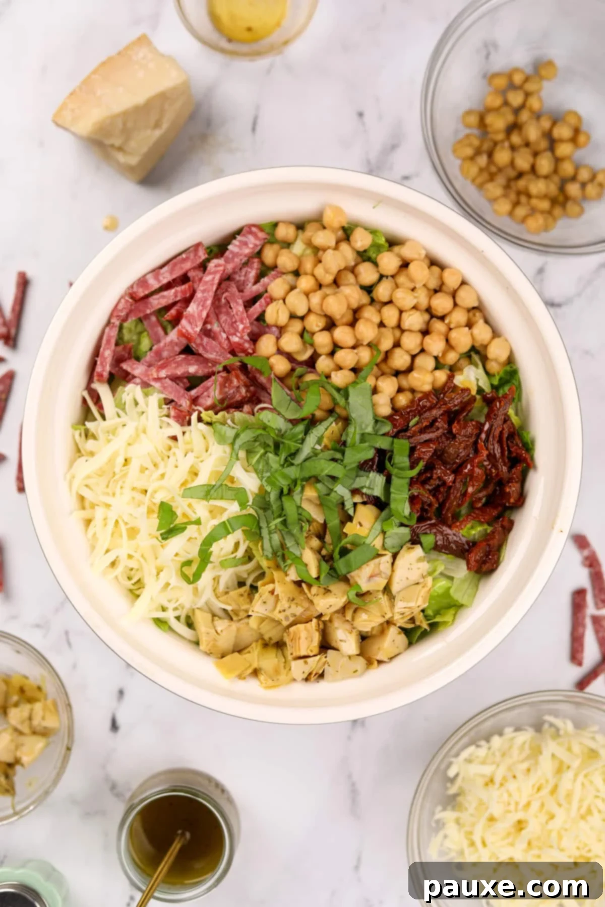 A large salad bowl with sections of colorful toppings arranged on top of the lettuce, including mozzarella, artichokes, basil, sun-dried tomatoes, chickpeas, and salami.