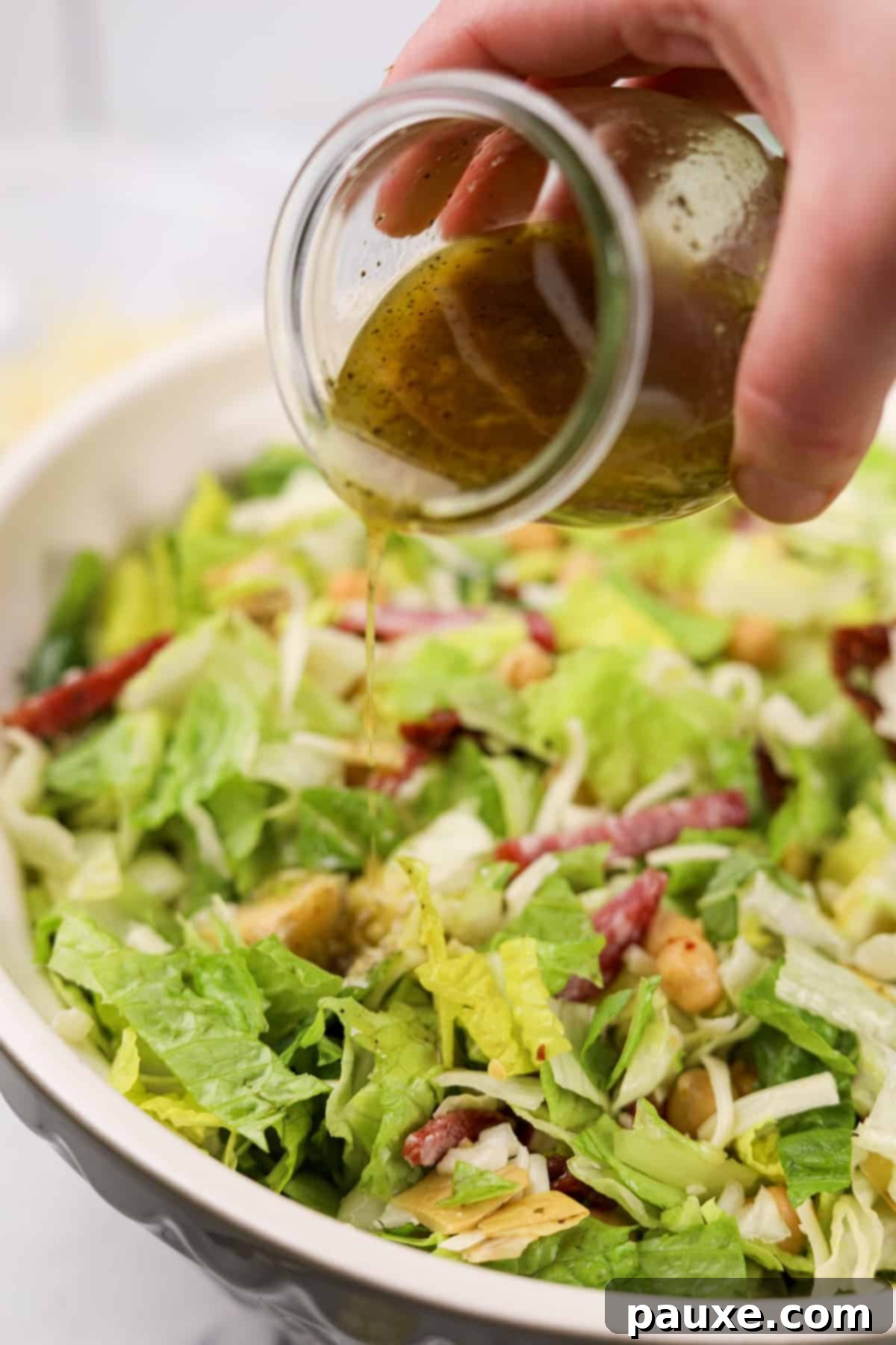 Pouring the homemade Leon dressing generously over the large bowl of chopped salad.