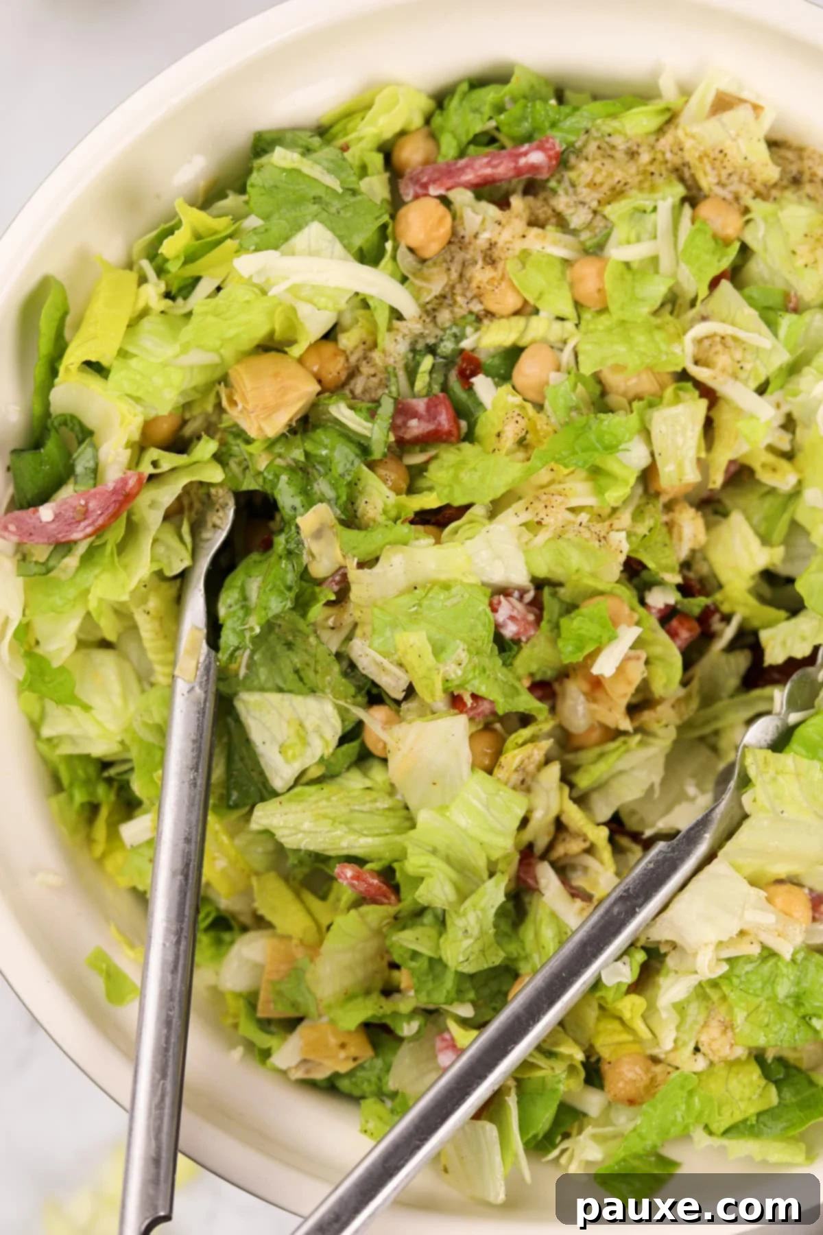 A pair of tongs actively tossing the chopped salad with the dressing, ensuring every piece is coated.