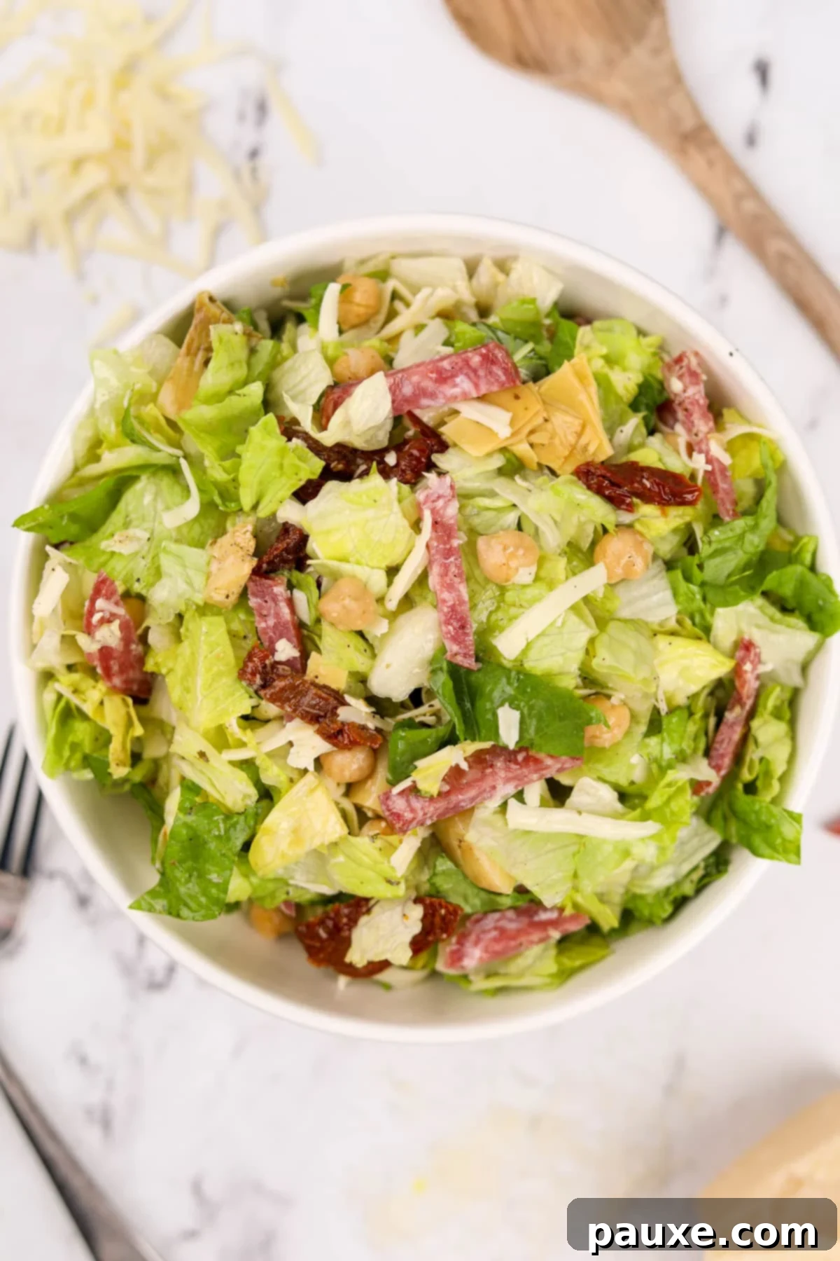 A beautifully presented large bowl of chopped Italian Salad, prominently featuring generous slices of salami and creamy mozzarella.