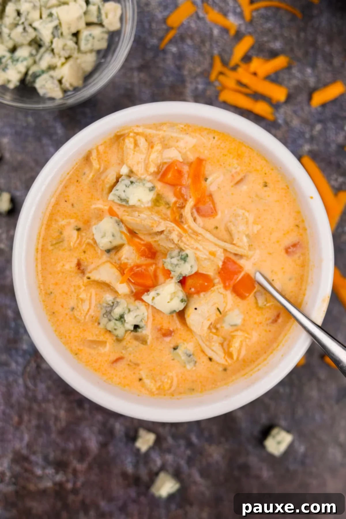 Spicy Buffalo Chicken Chowder 6 A vibrant bowl of buffalo chicken soup, generously topped with blue cheese crumbles, on a rustic wooden surface.