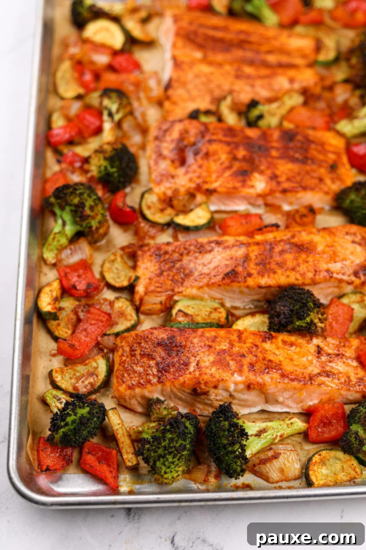 A sheet pan filled with roasted vegetables and salmon fillets.
