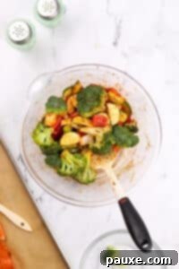 A large bowl with seasoned vegetables being stirred.