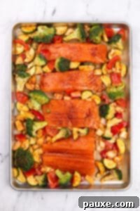 A sheet pan with seasoned salmon fillets and various vegetables.