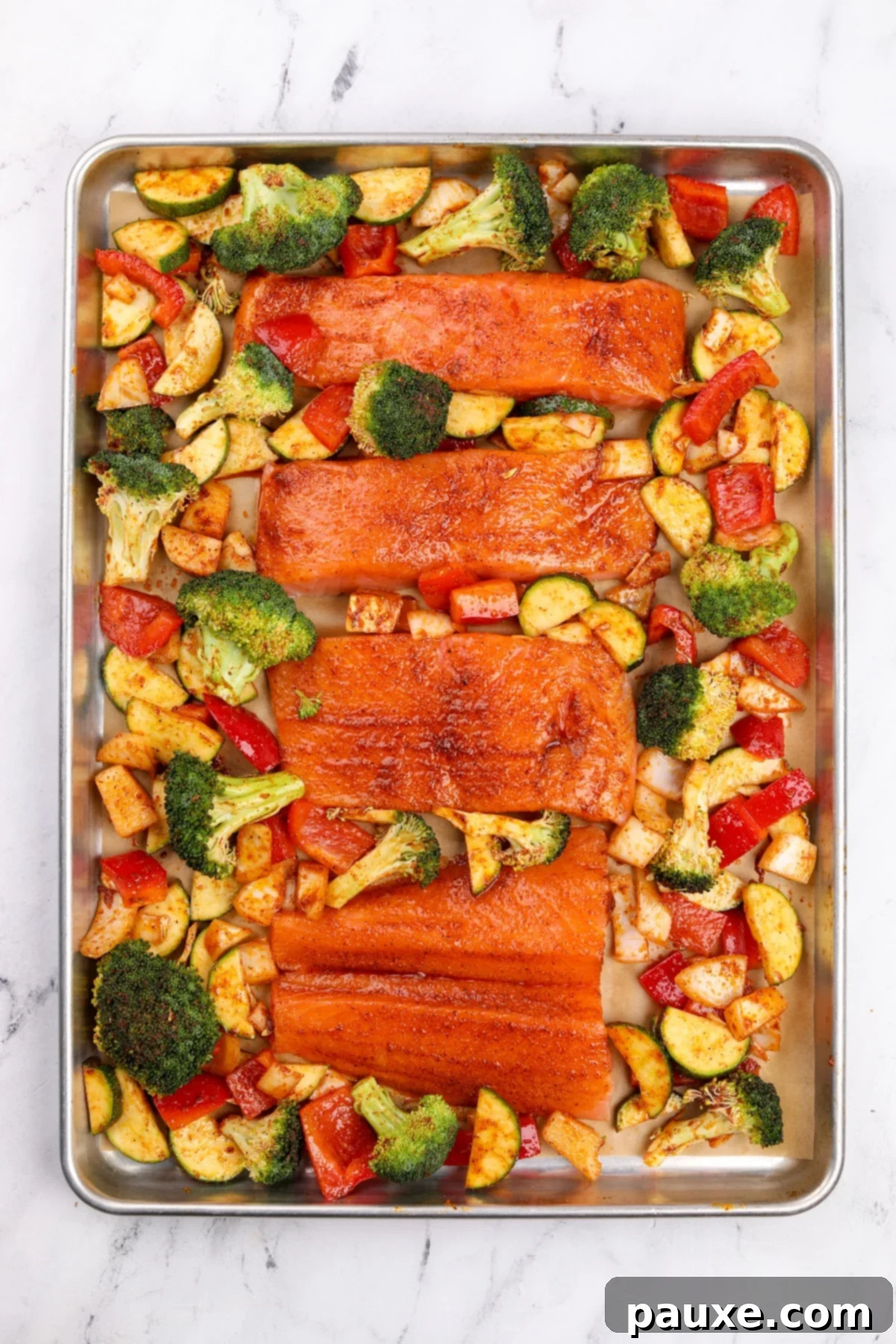 A sheet pan with seasoned salmon fillets and various vegetables.