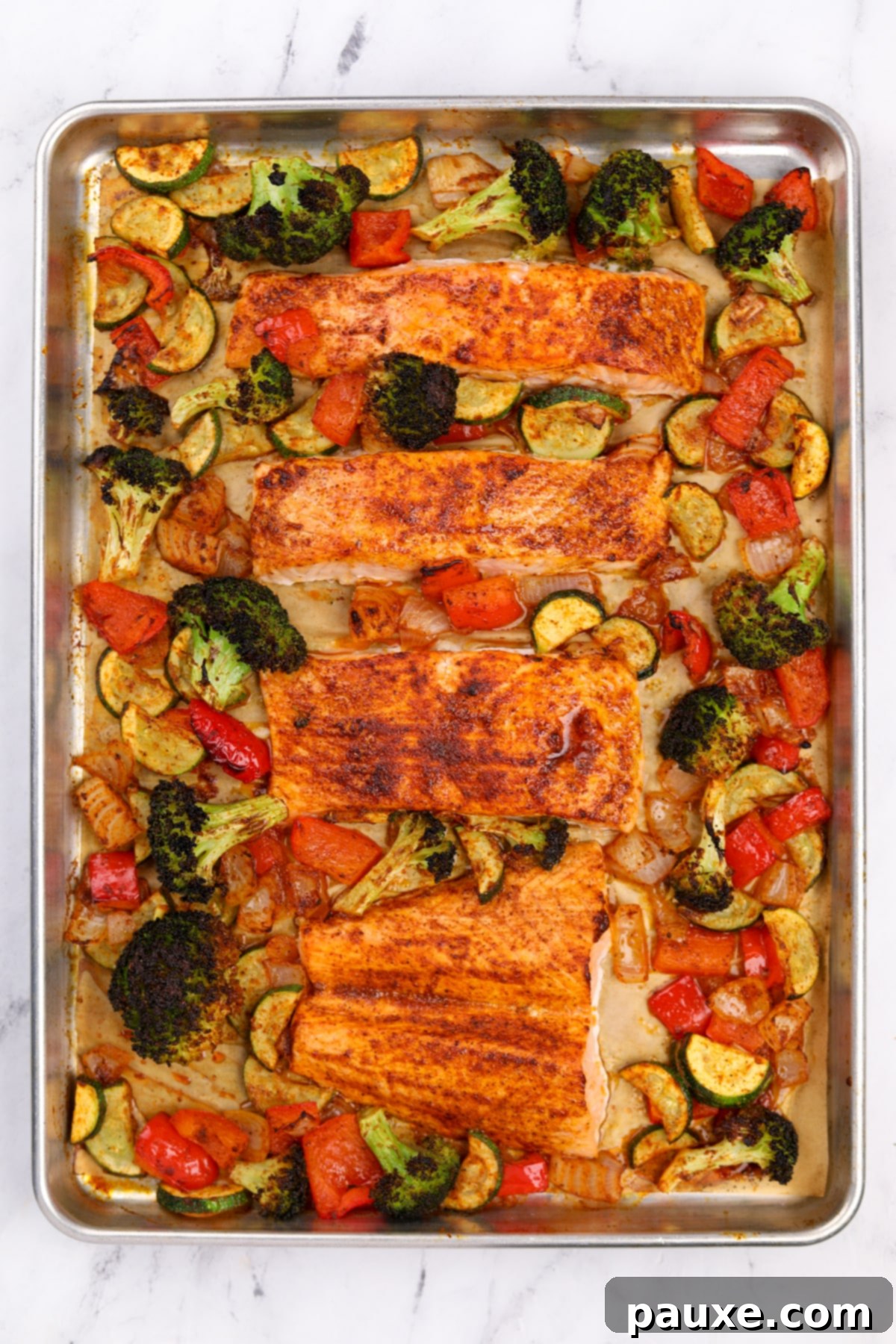 A sheet pan with roasted vegetables and salmon fillets.