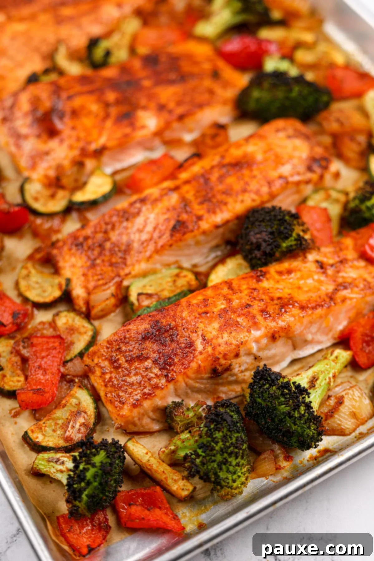 Seasoned salmon fillets surrounded by roasted vegetables on a baking sheet.