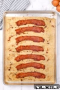 Perfectly Crispy Oven Bacon 11 Crispy cooked bacon slices on a baking sheet after being removed from the oven.