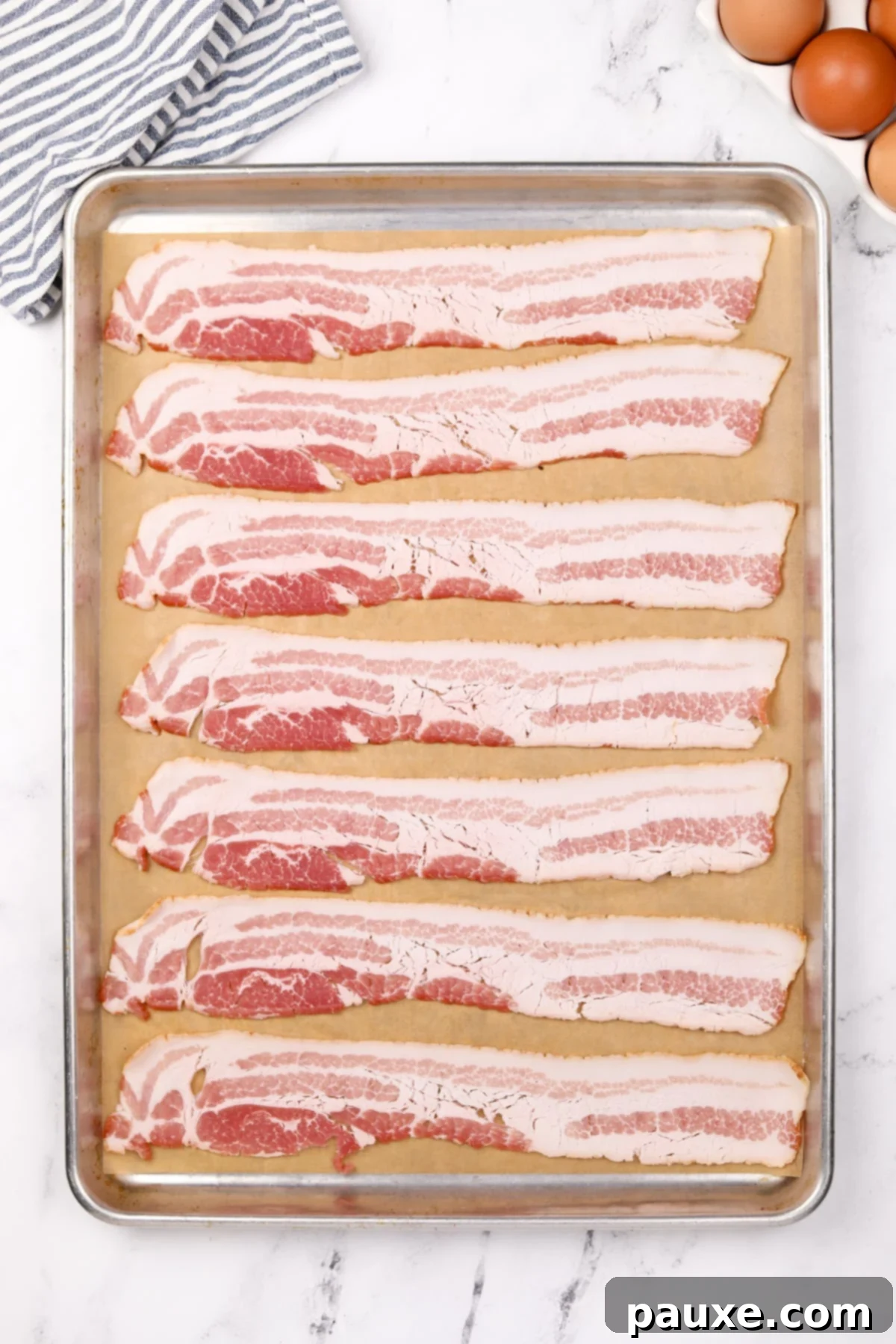 Perfectly Crispy Oven Bacon 4 Eight slices of uncooked bacon arranged in a single layer on a parchment-lined baking sheet, with ample space between each strip.