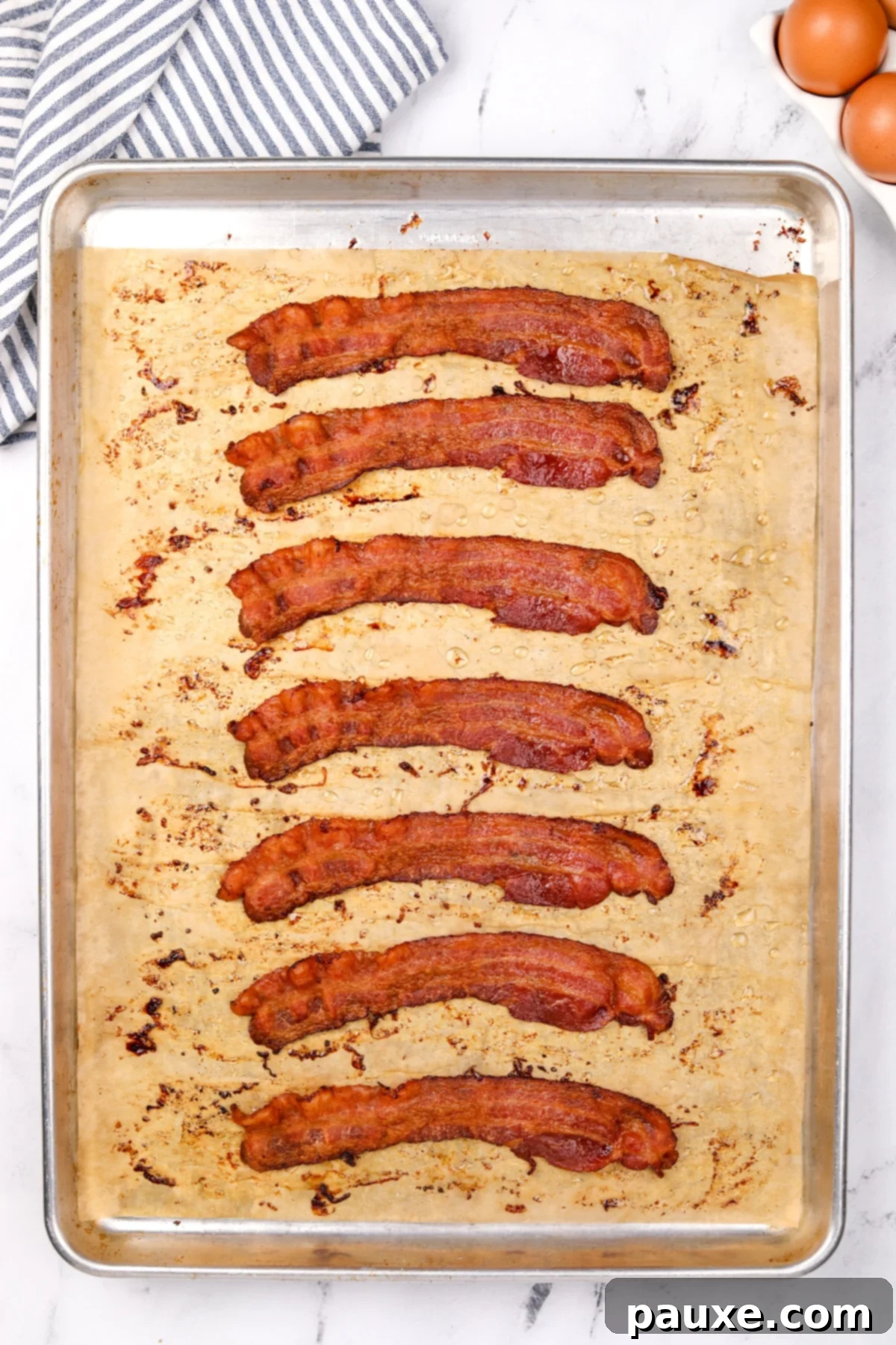 Perfectly Crispy Oven Bacon 5 A baking sheet featuring eight slices of perfectly cooked bacon, golden brown and crispy, ready to be removed from the oven.