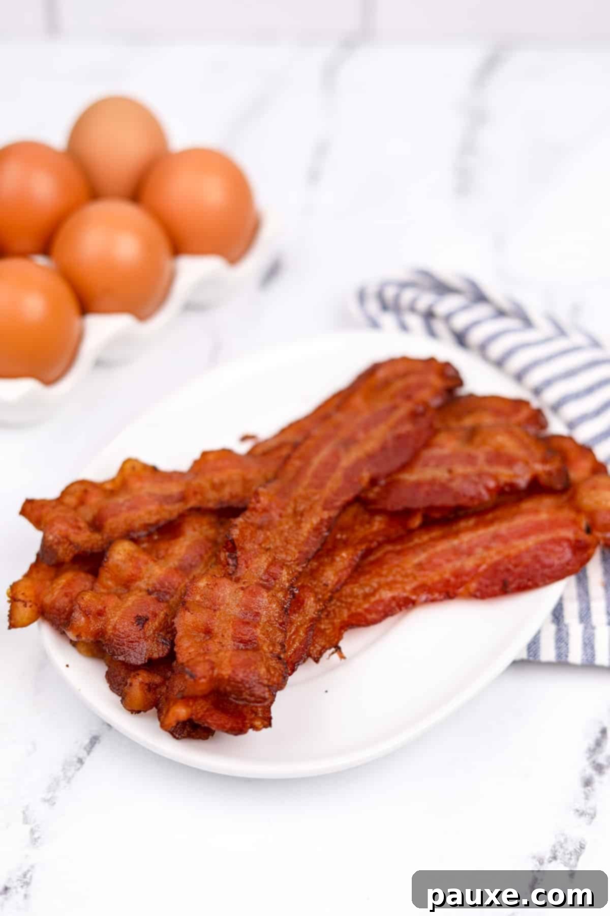 Perfectly Crispy Oven Bacon 6 A pristine white plate generously piled high with golden-brown, crispy bacon pieces, glistening and ready to be served.