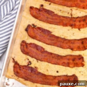 Perfectly Crispy Oven Bacon 9 Slices of crispy bacon on a parchment lined baking sheet, golden brown and ready to serve.