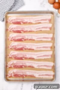 Perfectly Crispy Oven Bacon 10 Eight slices of bacon arranged on a parchment-lined baking sheet before cooking.