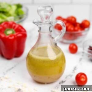 Zesty Mediterranean Vinaigrette 8 A glass cruet filled with homemade Greek salad dressing, with red pepper, tomatoes, and lettuce artfully blurred in the background.