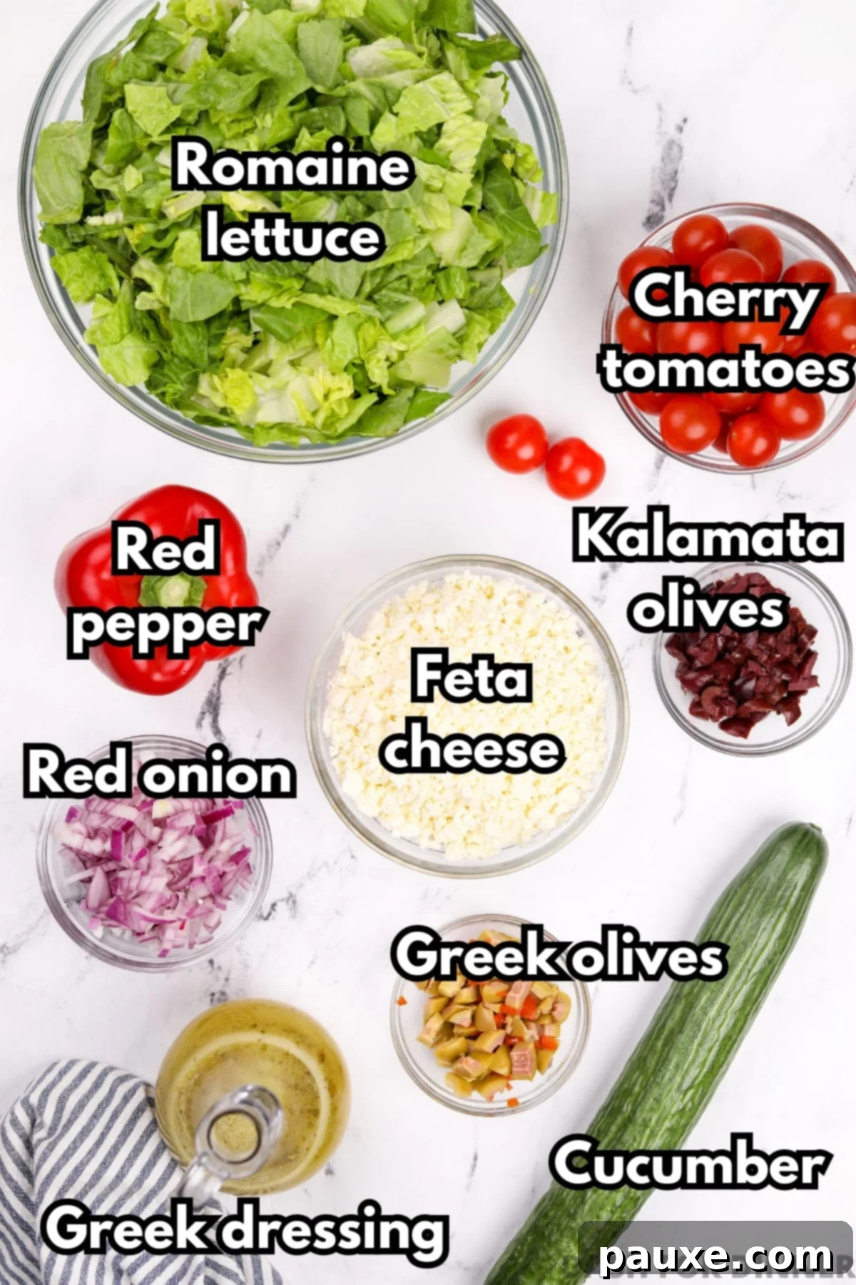 Vibrant Greek Chopped Salad 3 Various fresh ingredients laid out for a Greek salad, including a block of feta cheese, cherry tomatoes, cucumbers, red onion, Kalamata olives, a red bell pepper, and a bottle of Greek dressing.