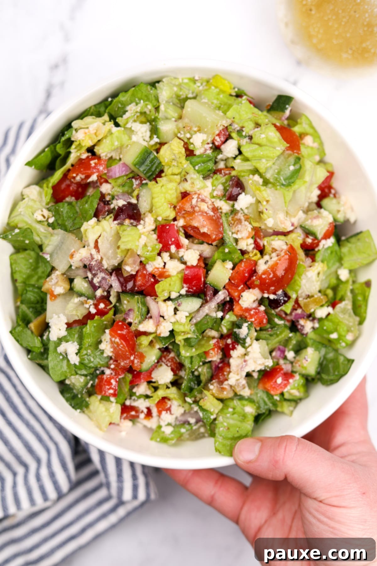 Vibrant Greek Chopped Salad 7 A person's hand holding a clear glass bowl filled with Greek chopped salad, showcasing the fresh ingredients.