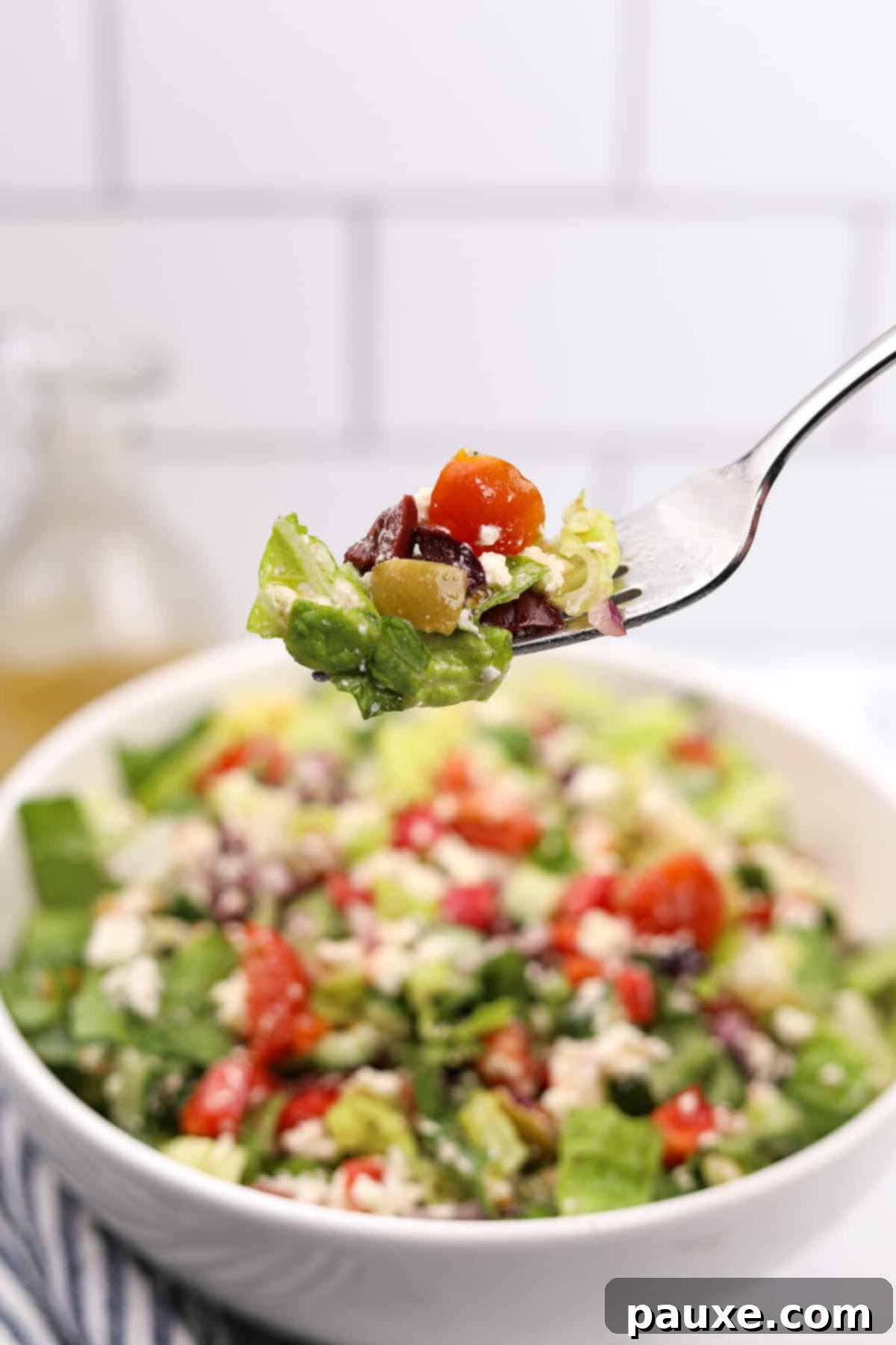 Vibrant Greek Chopped Salad 8 A fork lifting a portion of Greek chopped salad from a white bowl, showing a mix of lettuce, feta, tomatoes, and olives.