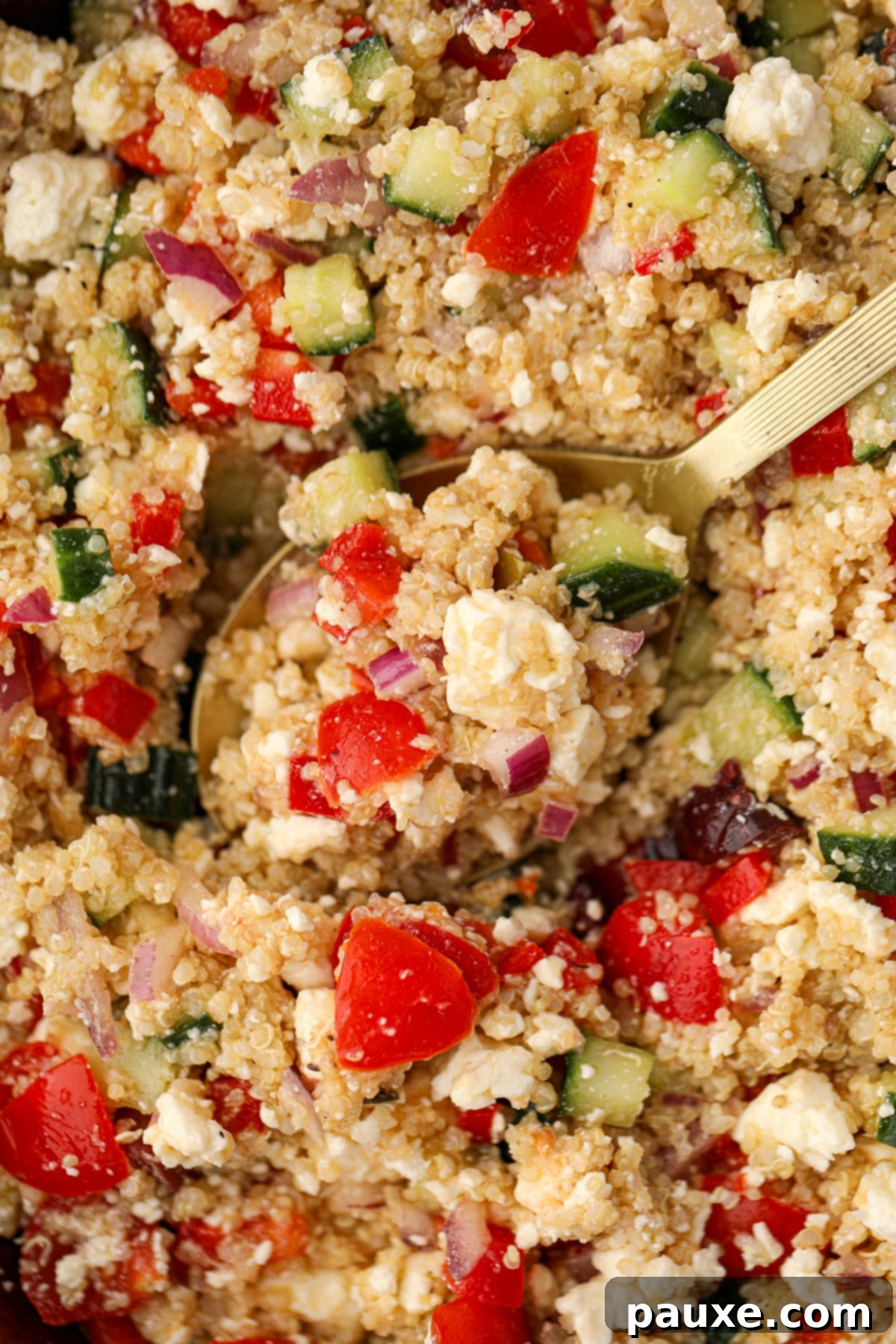 Zesty Mediterranean Quinoa Salad 6 A spoon expertly scooping a hearty portion of Greek Quinoa Salad, highlighting the visible pieces of red pepper, creamy feta, and crisp cucumbers.