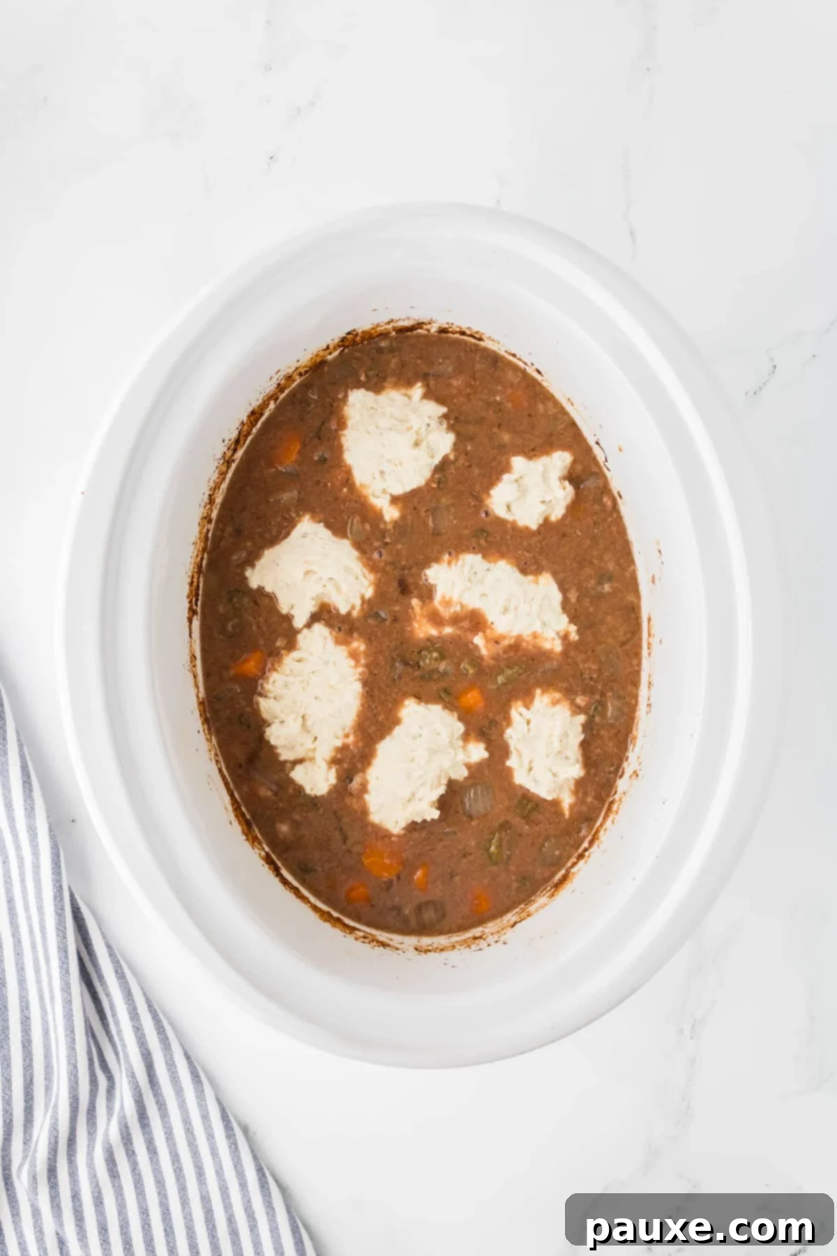 Comforting Slow Cooker Beef Stew and Dumplings 12 A slow cooker insert showing dumplings steaming on top of the beef stew, covered and cooking.