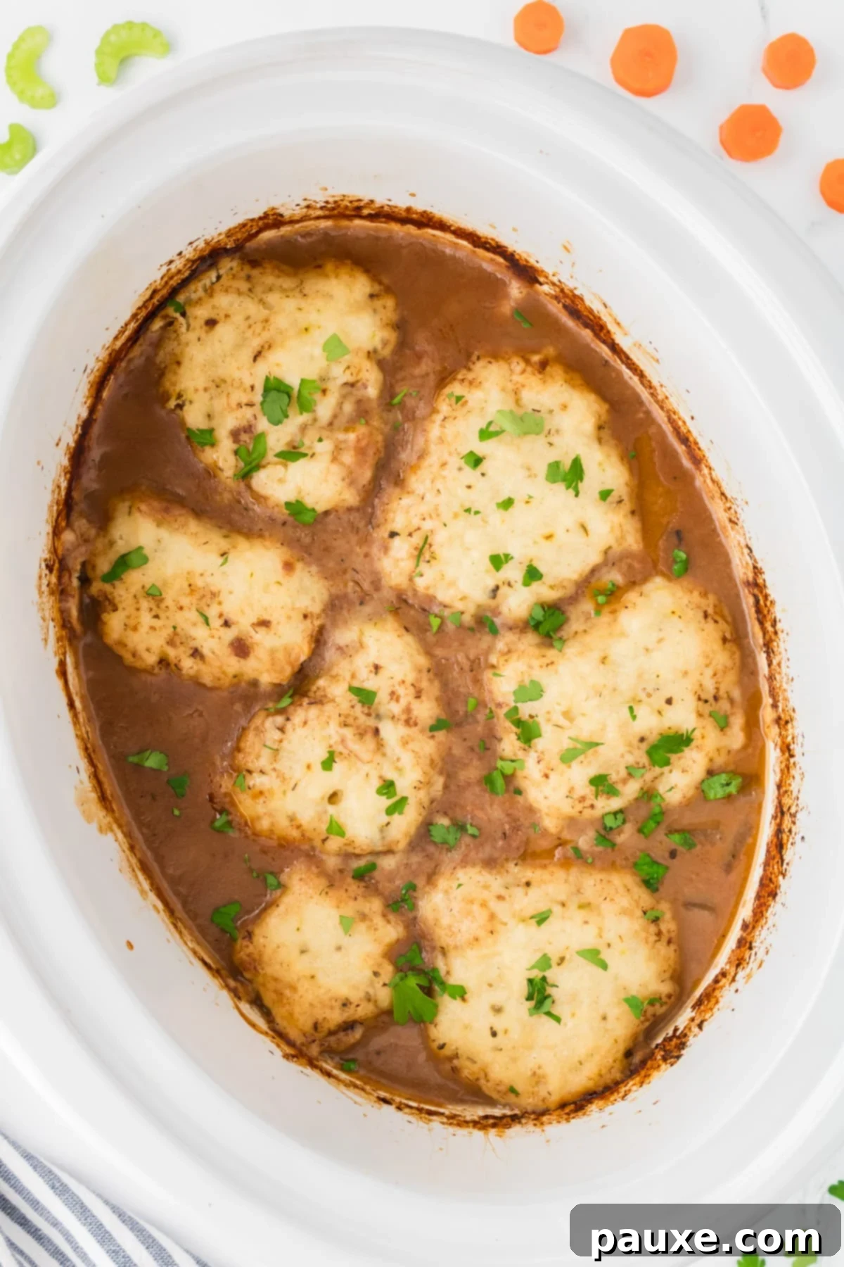 Comforting Slow Cooker Beef Stew and Dumplings 13 A white slow cooker insert filled with rich beef stew, beautifully topped with golden-brown homemade dumplings and fresh parsley.